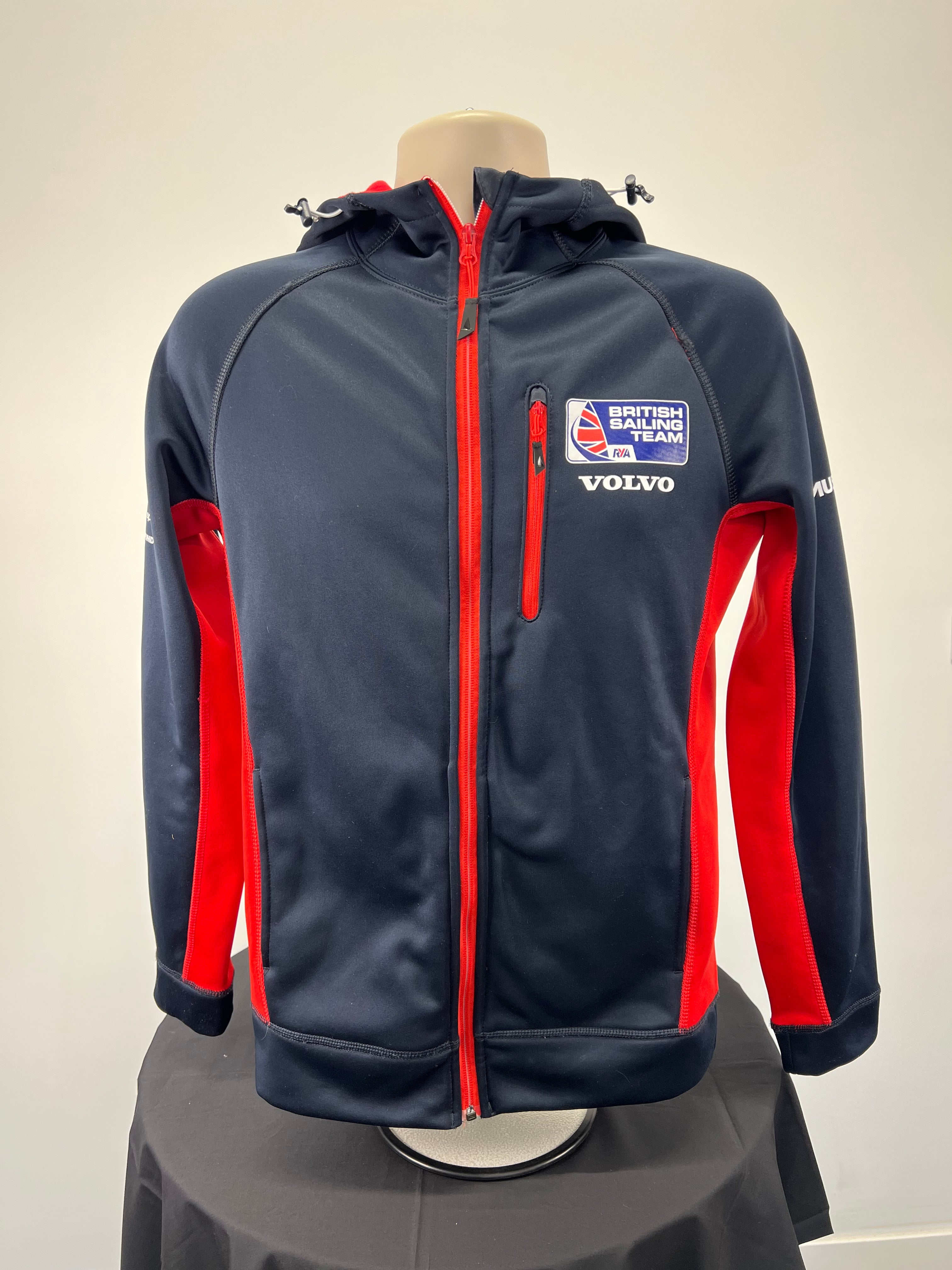 Front view of navy blue Musto British Sailing Team softshell jacket with red side panels and chest zipper pocket