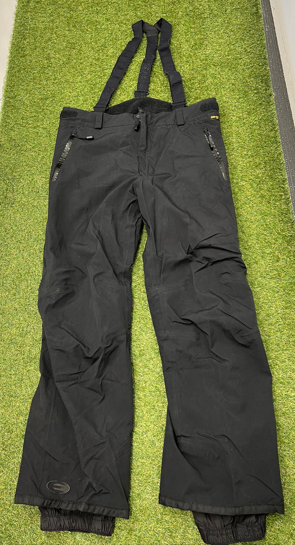 Men’s black Eider ski trousers with adjustable braces laid flat on grass showing front view