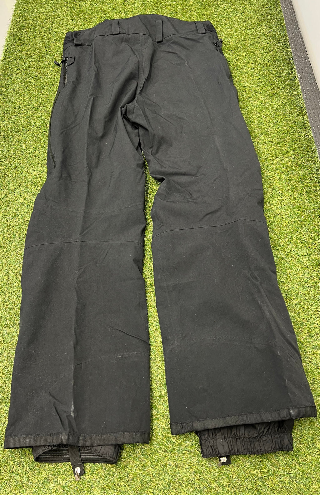Back view of men’s black ski trousers with adjustable braces laid flat on grass