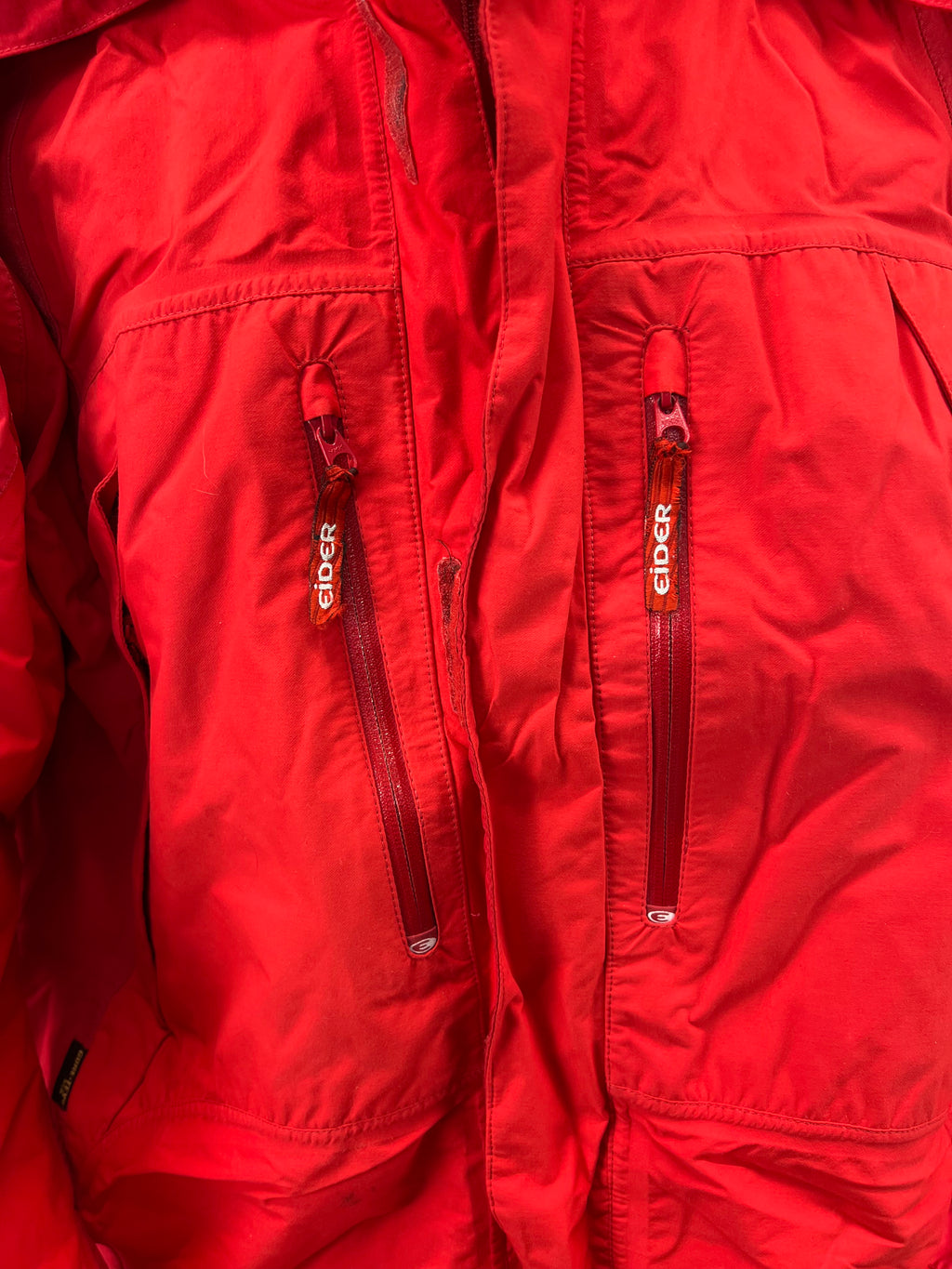 Close-up of two front vertical zippered pockets on red Eider jacket with branded zipper pulls