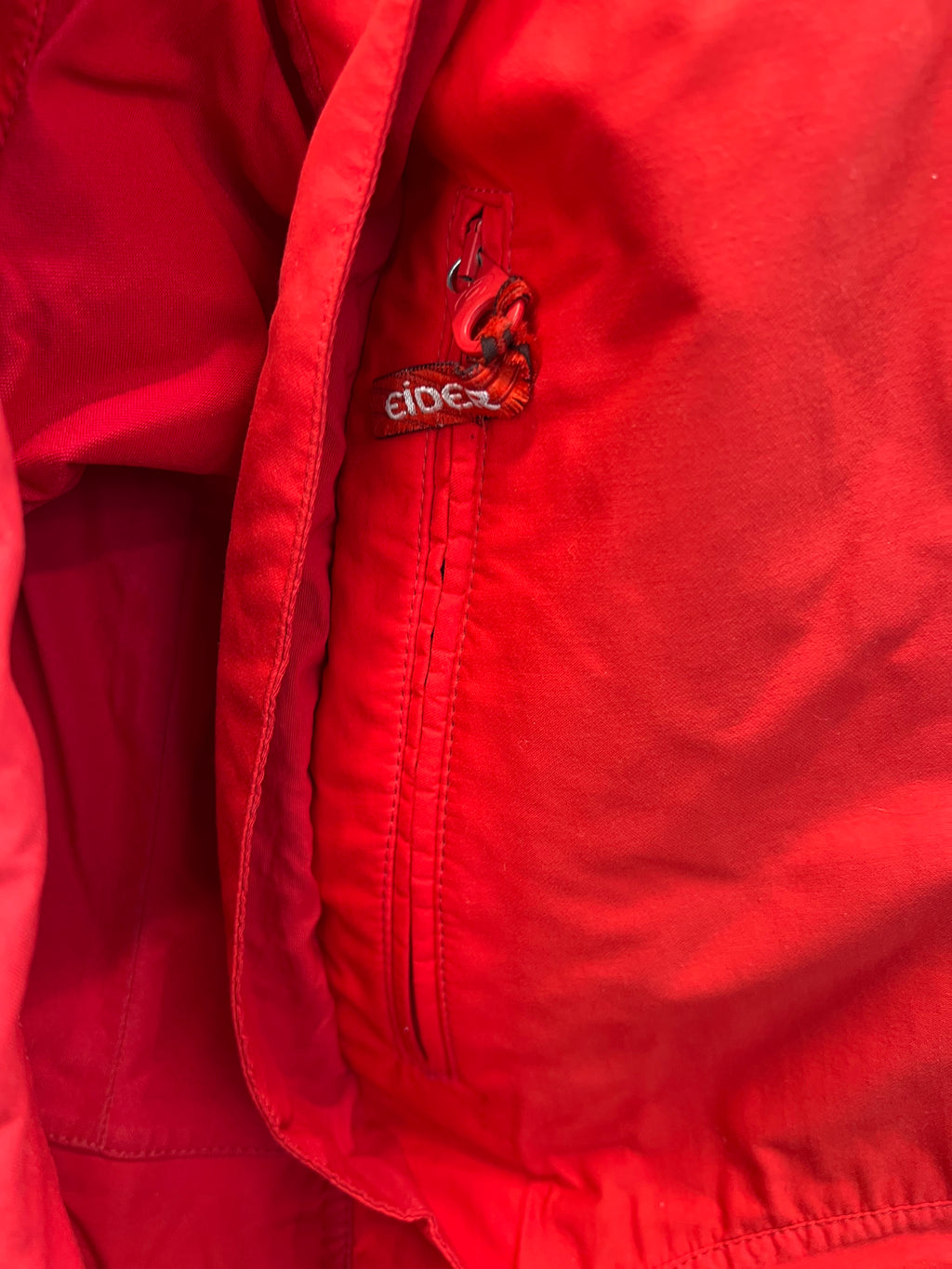 Close-up of inner pocket zipper detail with Eider branding on red jacket