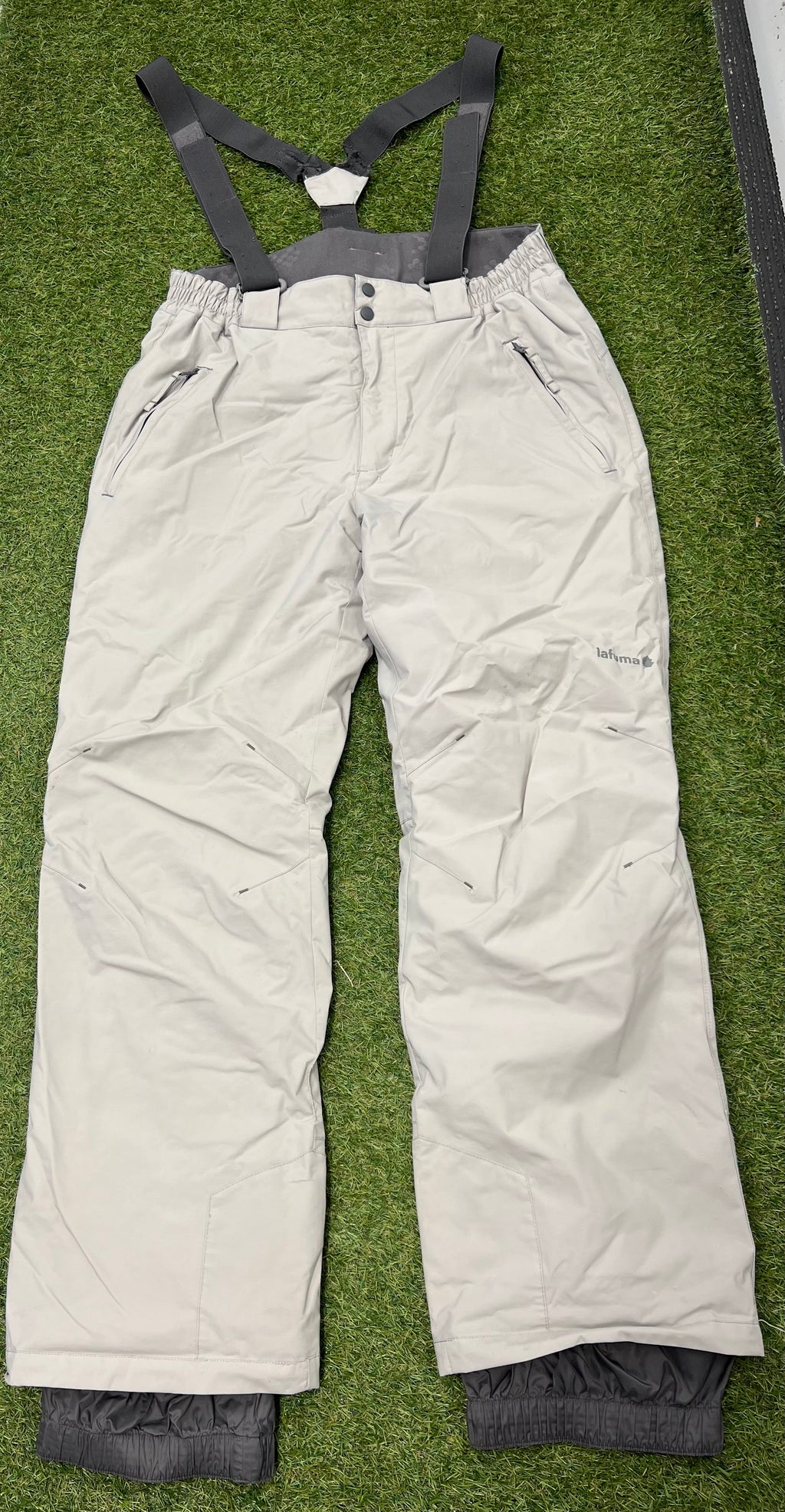 Front view of light grey Lafuma insulated ski trousers with black adjustable braces laid flat on grass
