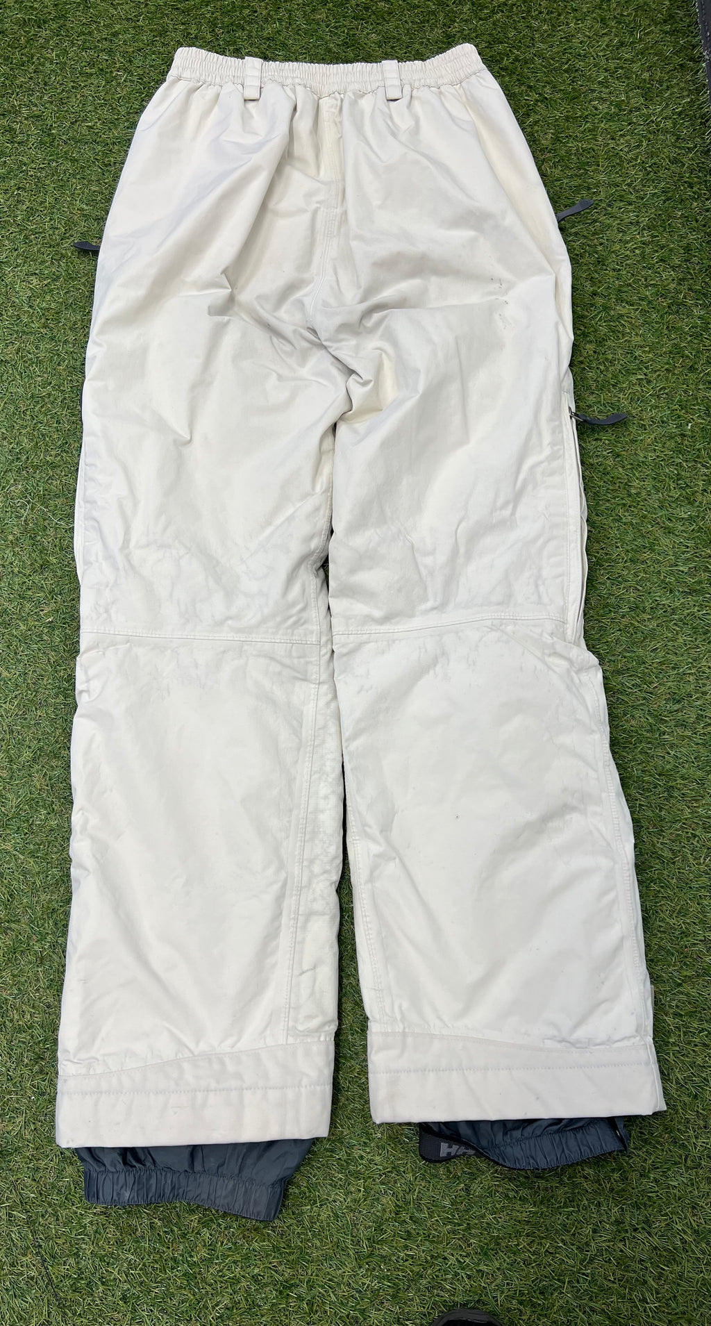 Back view of cream Helly Hansen women's ski trousers laid flat on grass highlighting elasticated waistband and rear stitching