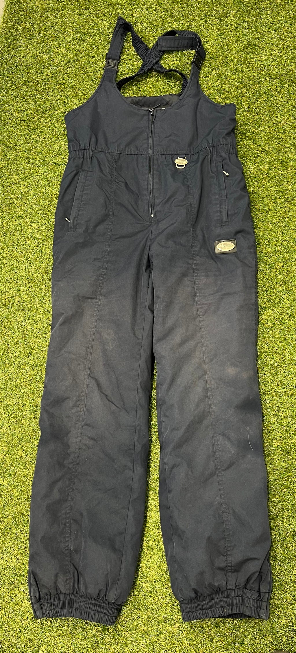 Front view of black Campri Ski Action insulated salopettes with adjustable straps and elasticated ankle cuffs laid on grass background