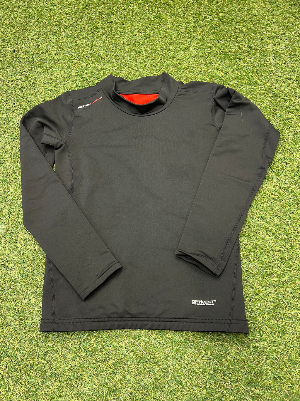 Back view of Sondico kids black long sleeve base layer top on green grass surface.