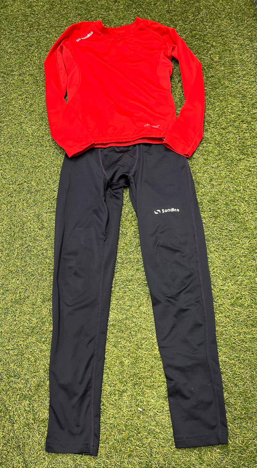 Red Sondico long sleeve base layer top paired with black Sondico leggings laid out on grass