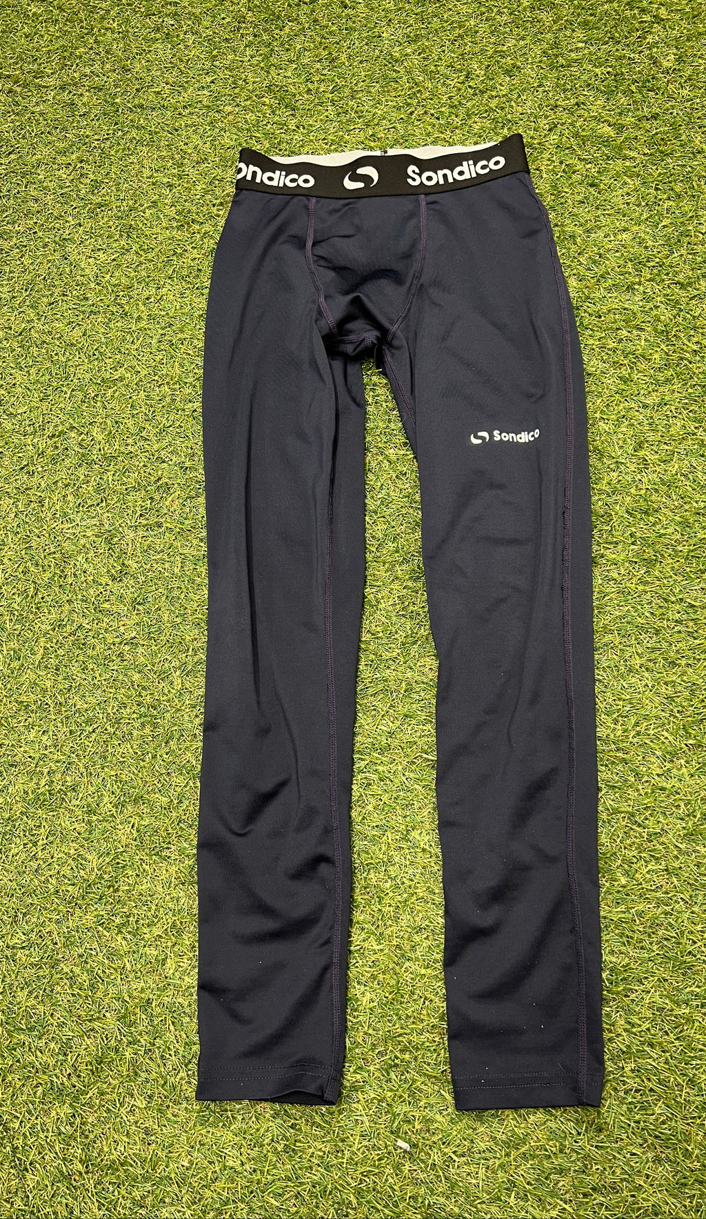 Black Sondico branded leggings shown flat on grass highlighting the front elastic waistband