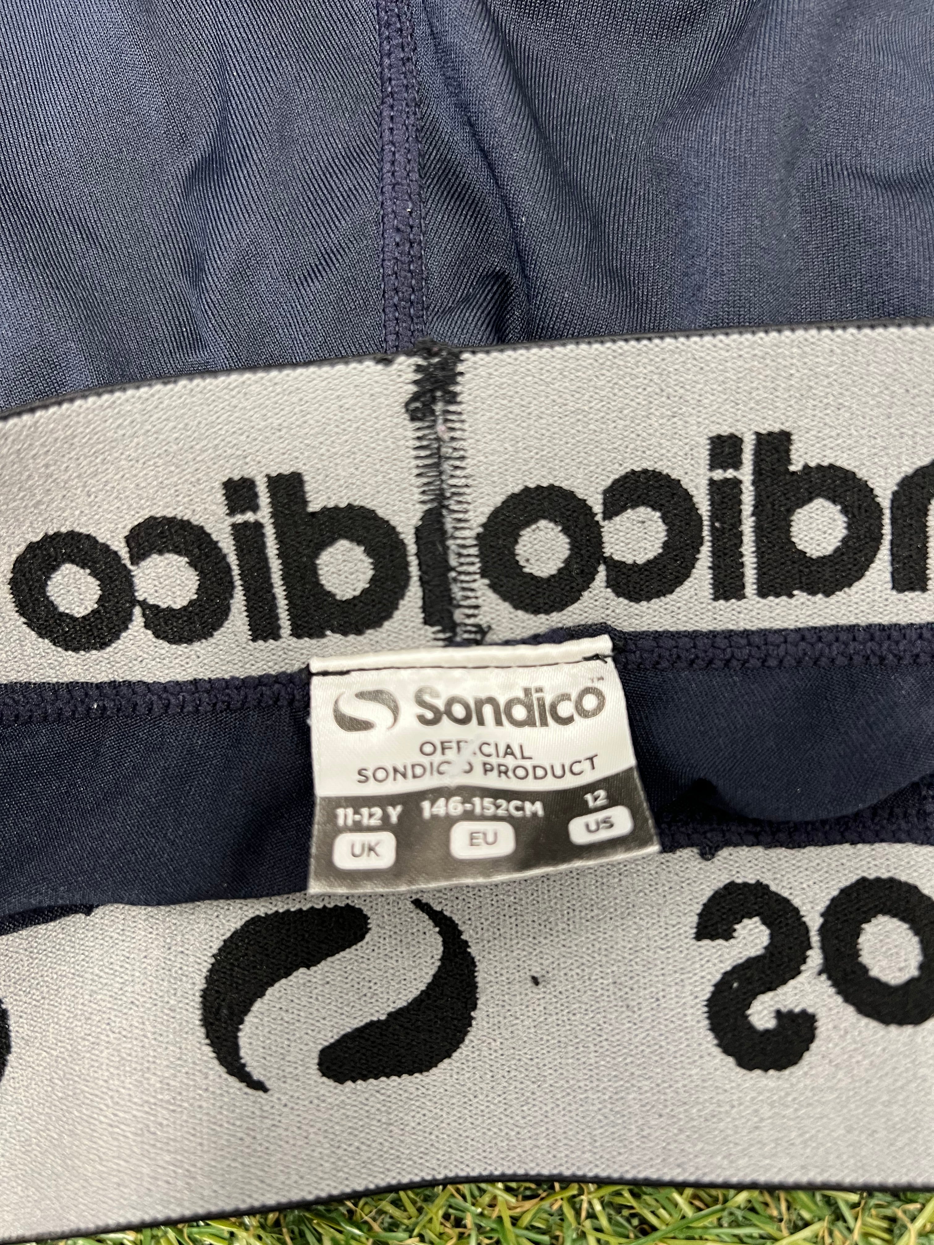 Sky blue Sondico long-sleeve base layer top with breathable beige mesh side panels shown from the front on grass