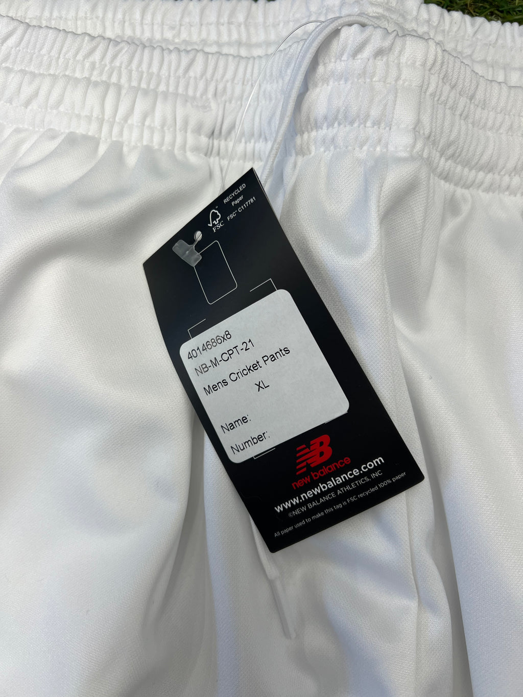 Close-up of black tag attached to white cricket trousers with size XL label and New Balance logo