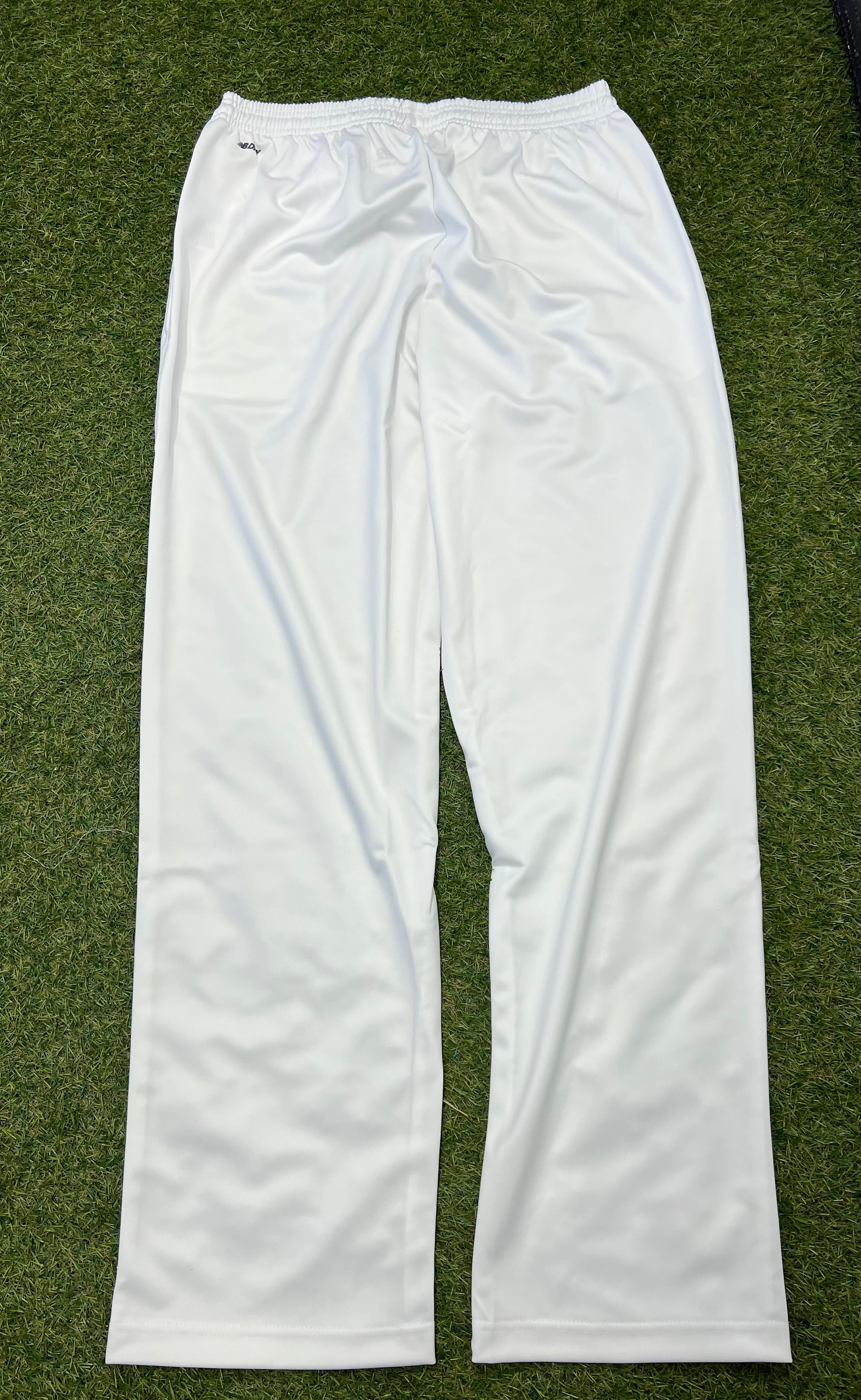 Back view of white New Balance men's cricket trousers laid flat on grass