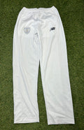 Front view of New Balance Hampshire Cricket Club white cricket trousers with logo on green grass