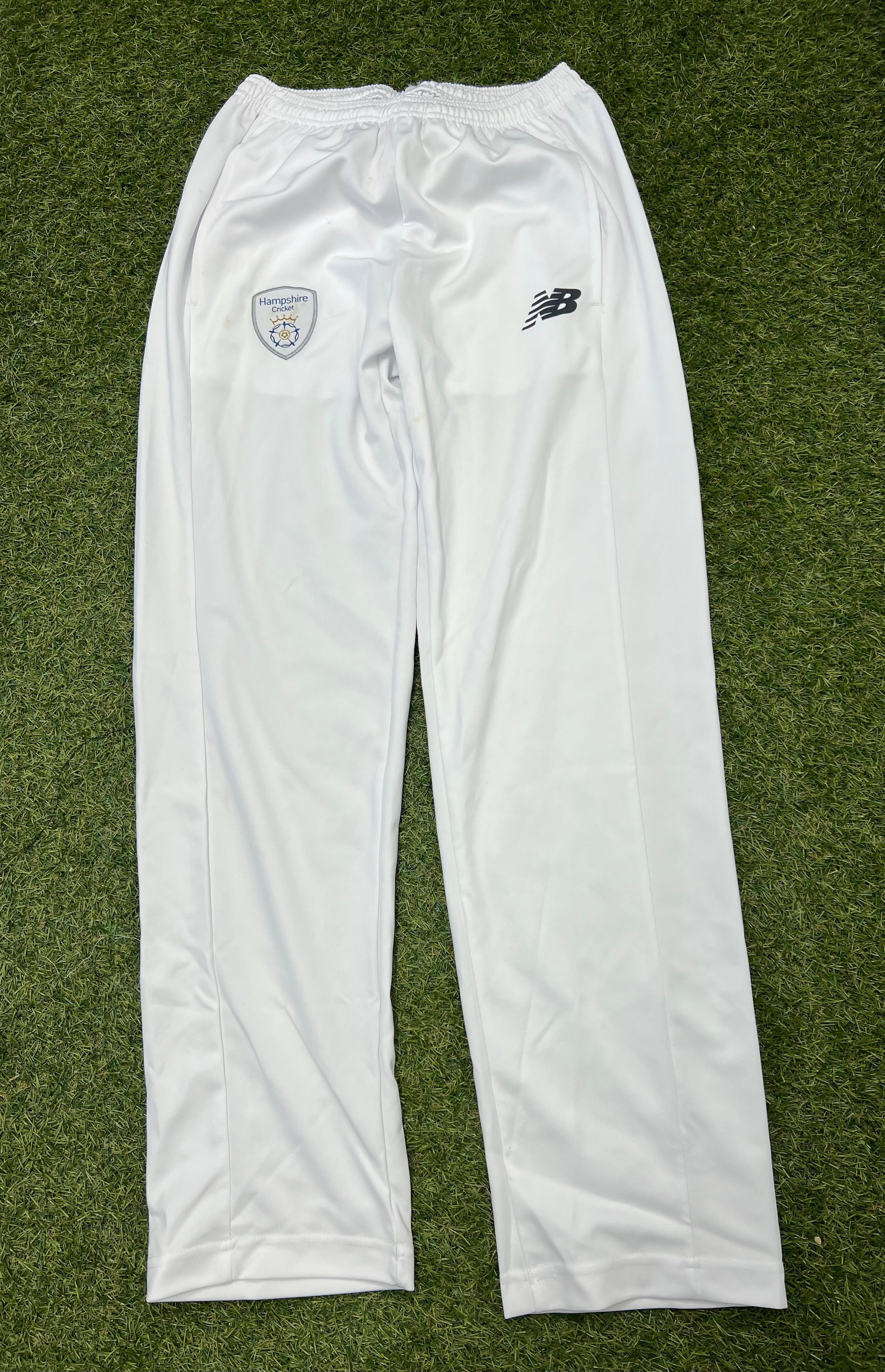 Front view of white New Balance cricket trousers with Hampshire Cricket Club badge and logo on green grass