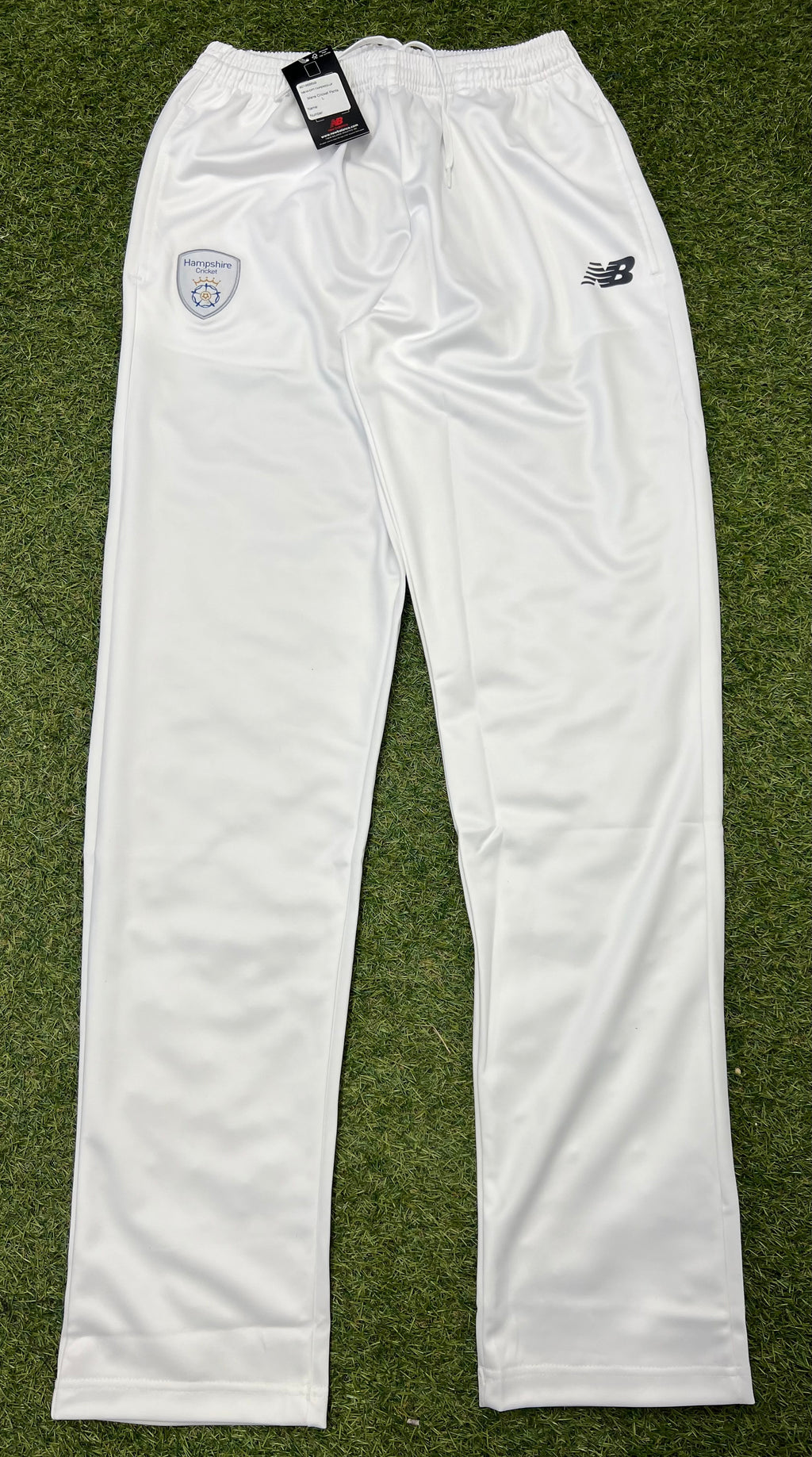Front view of white New Balance Hampshire Cricket Club men's tapered cricket trousers on grass