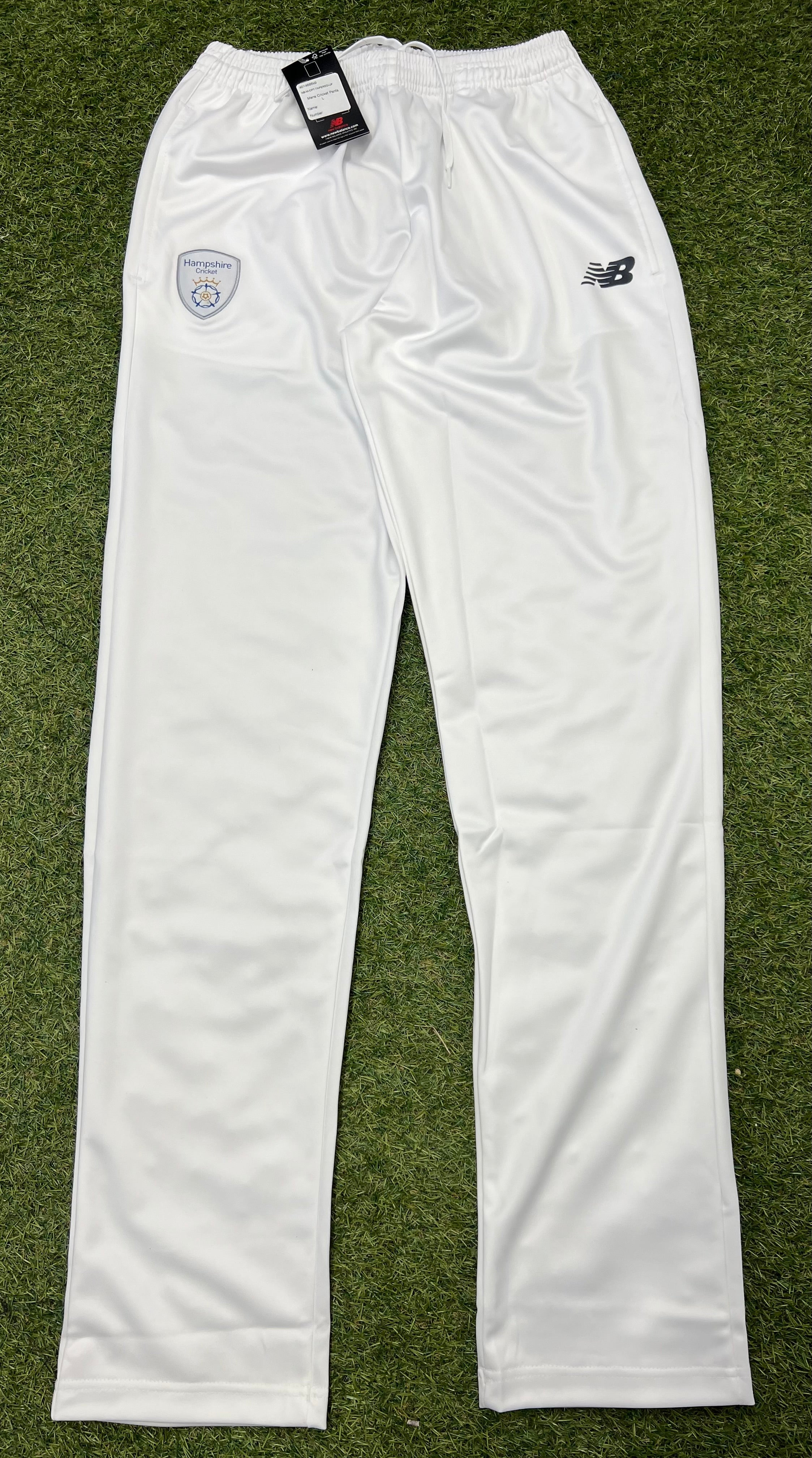Front view of white New Balance Hampshire Cricket Club men's tapered cricket trousers on grass