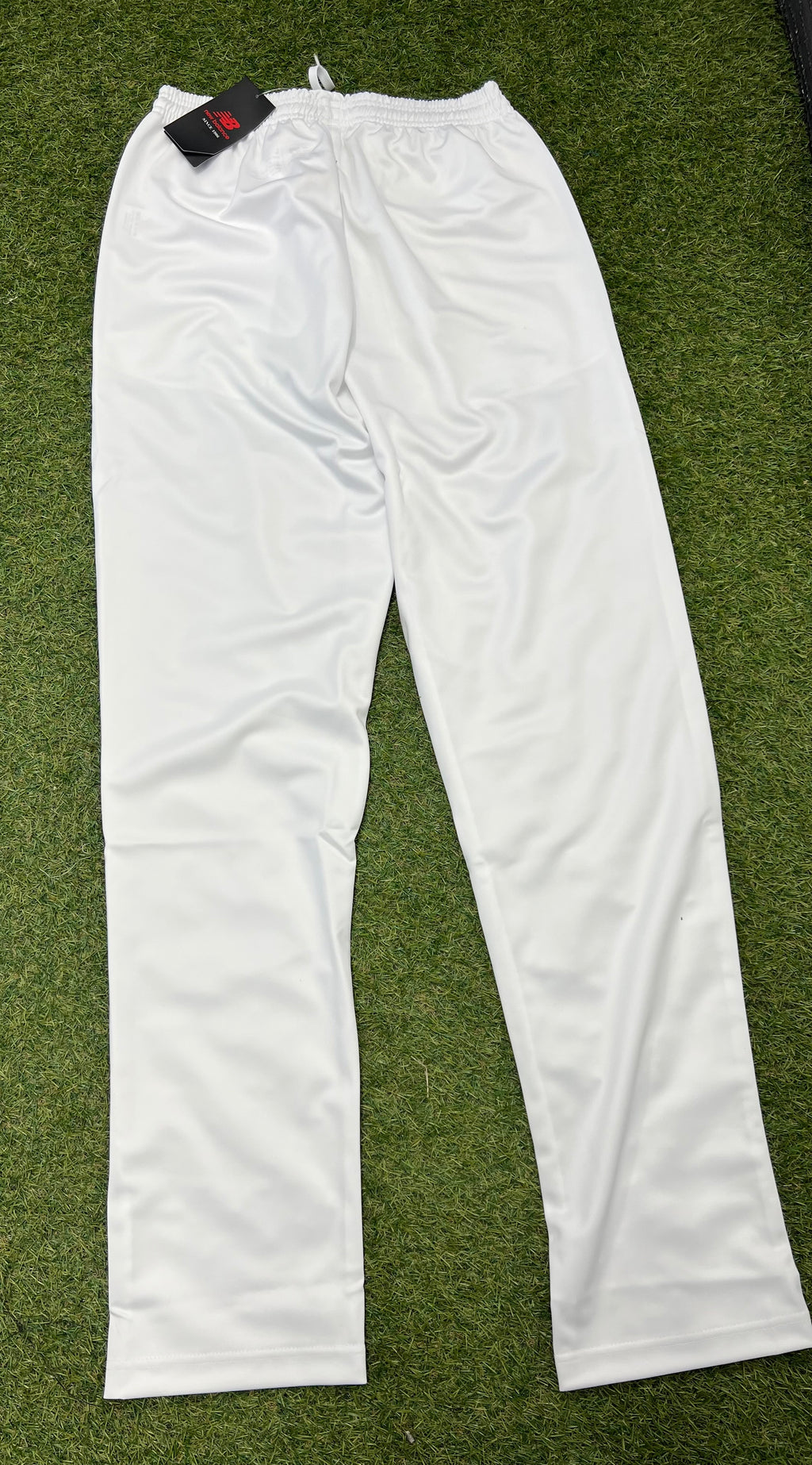Rear view of white New Balance men's cricket trousers laid on grass showing tapered leg design