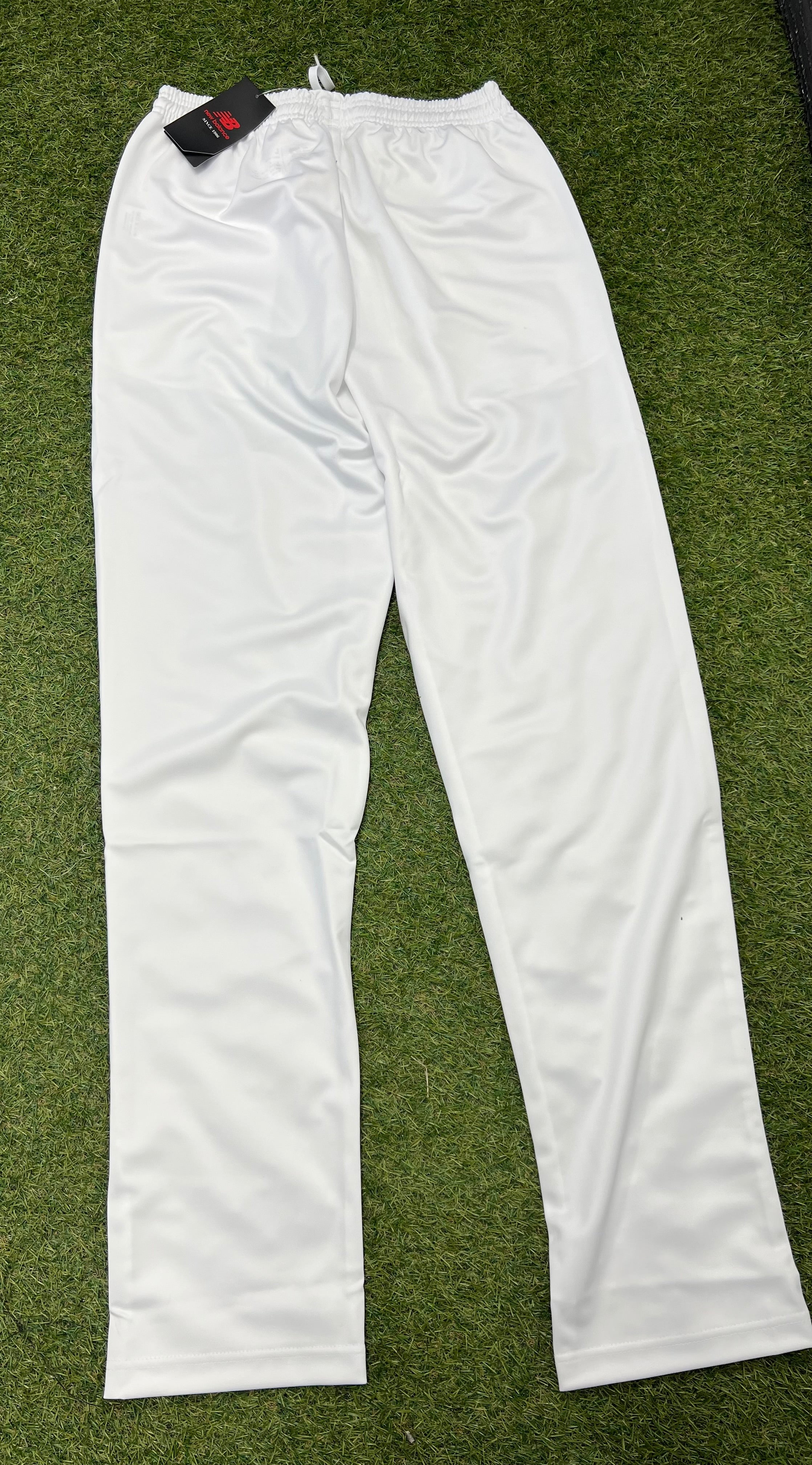 Rear view of white New Balance men's cricket trousers laid on grass showing tapered leg design