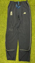 Front view of New Balance navy cricket tracksuit bottoms with white piping and embroidered logos