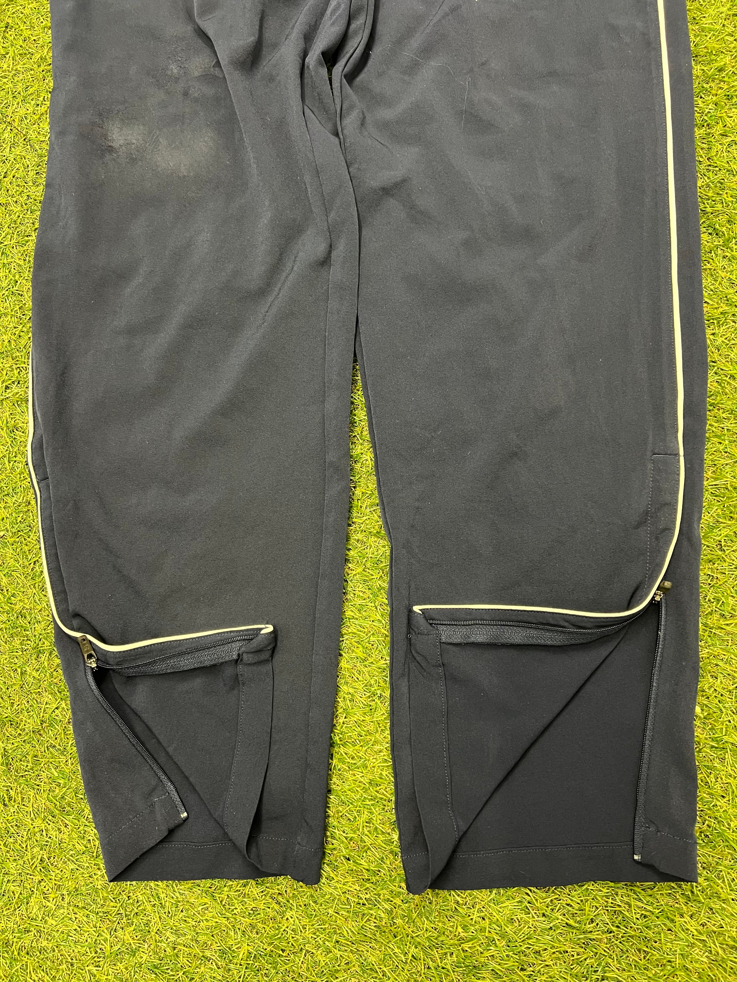 Close-up of zippered ankle vents on black tracksuit bottoms with yellow piping detail
