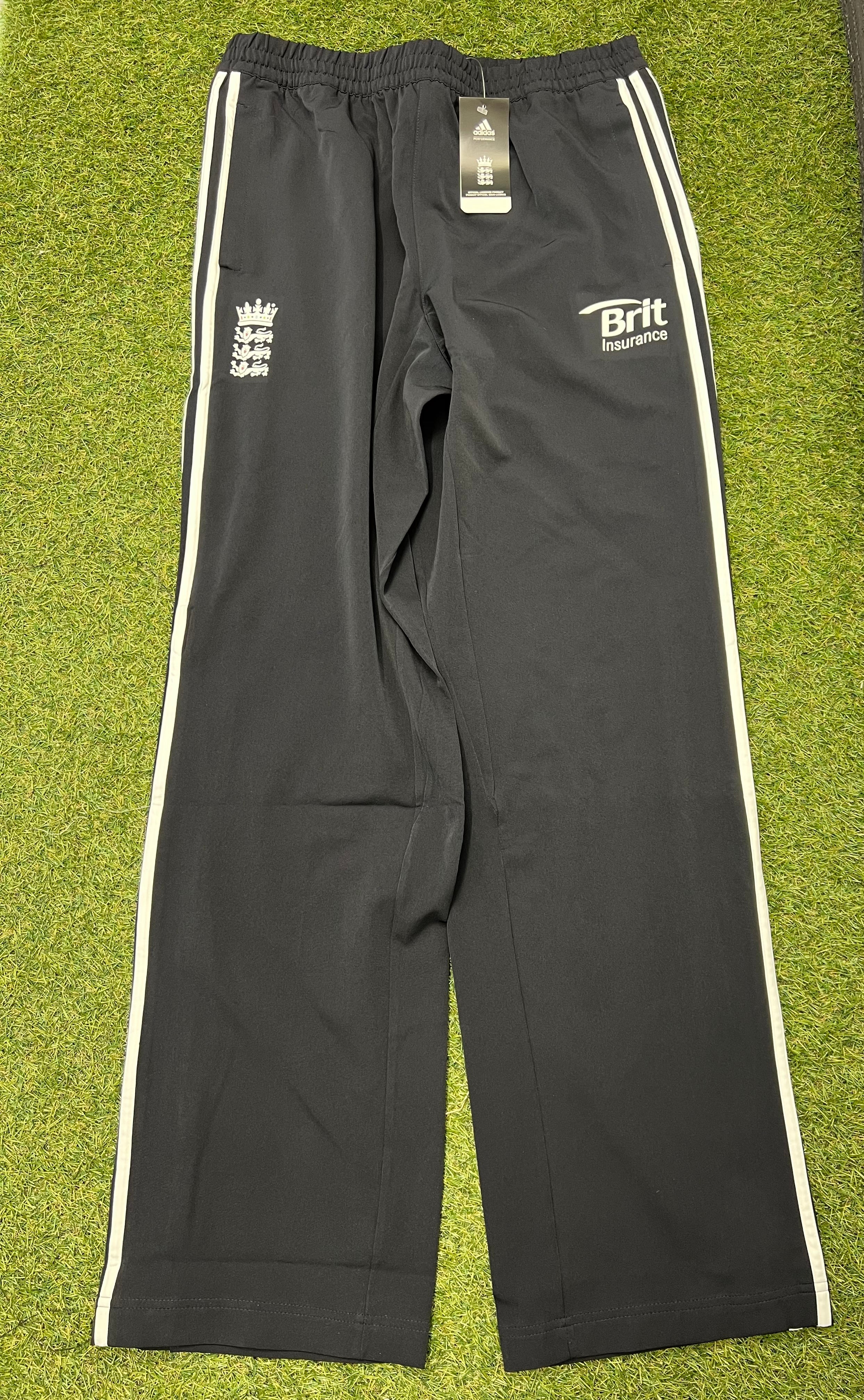 Front view of black Adidas cricket training trousers with white stripes and England Cricket Board logo on grass background