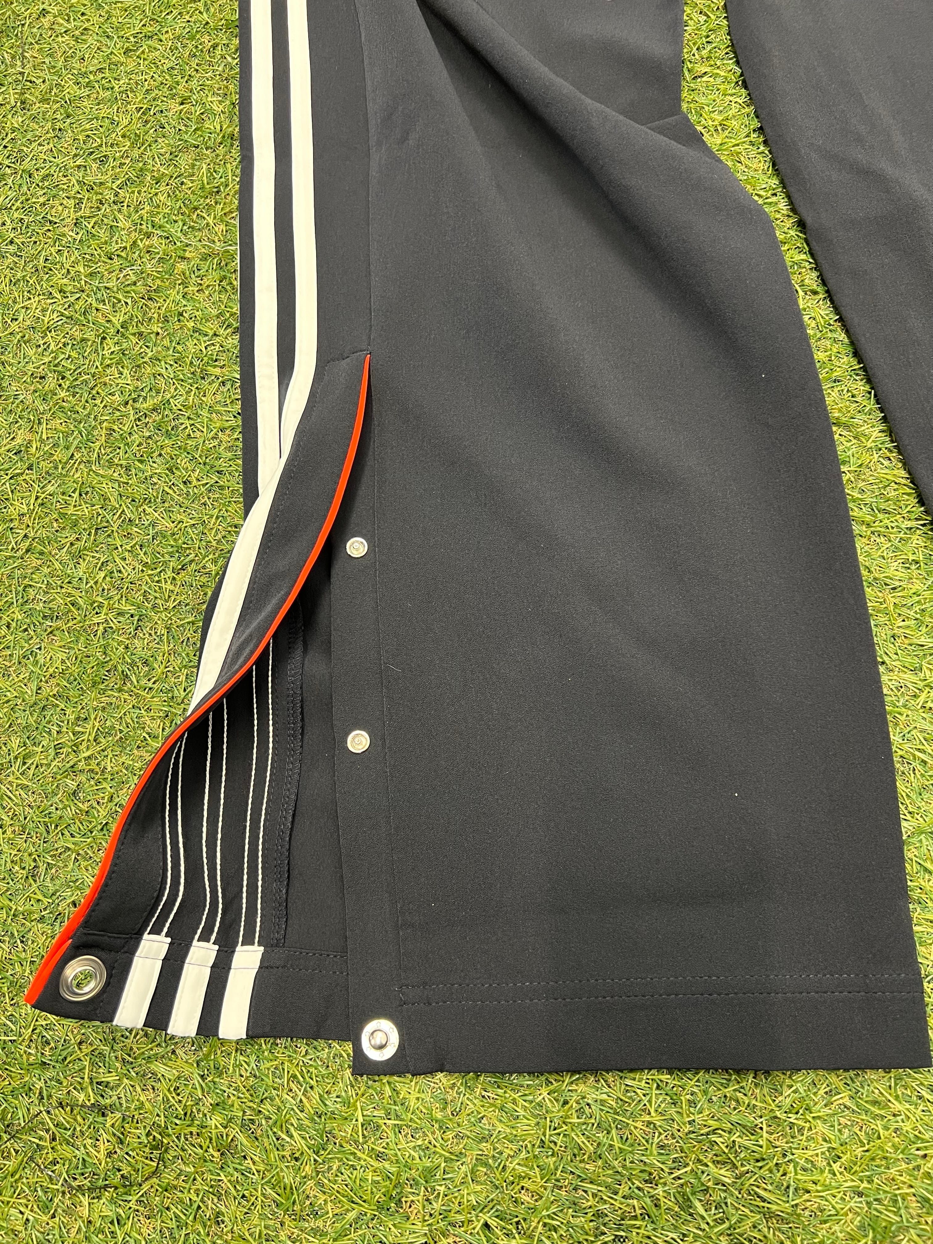 Close-up of ankle snap fasteners opened on black Adidas training trousers with white stripes and red trim
