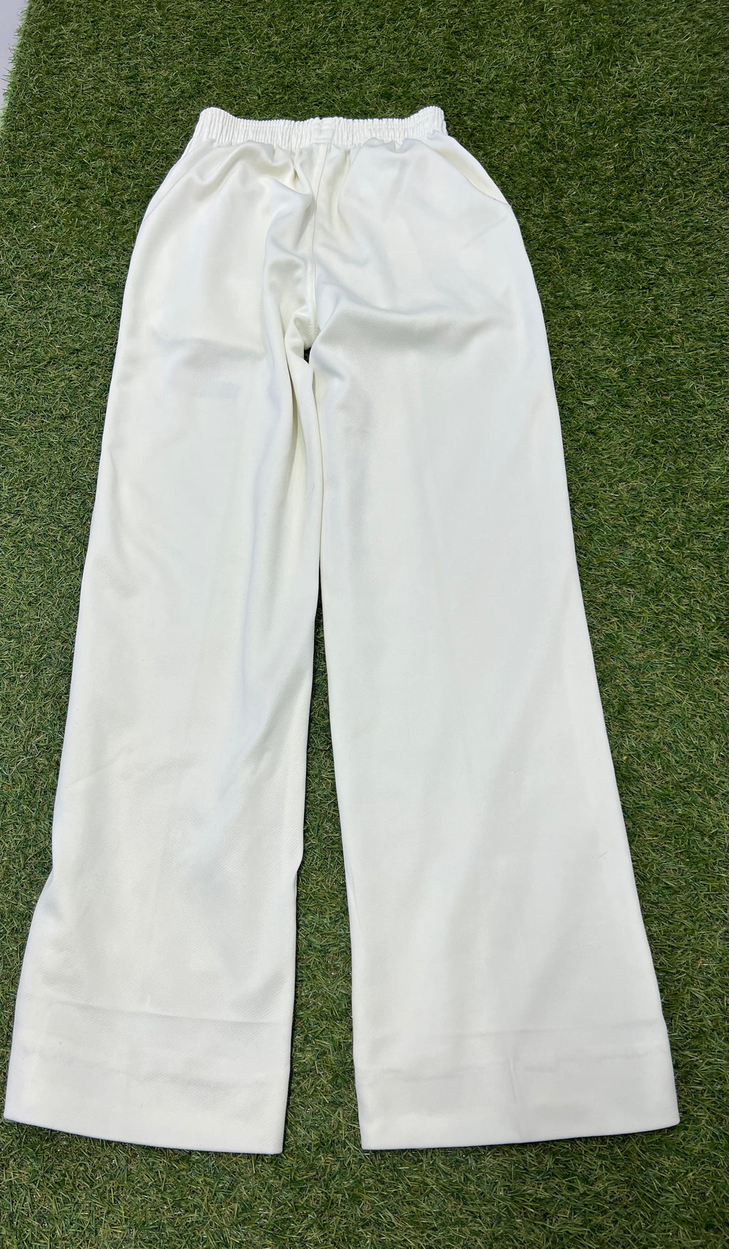 Back view of white cricket trousers showing elasticated waistband and plain rear on grass background