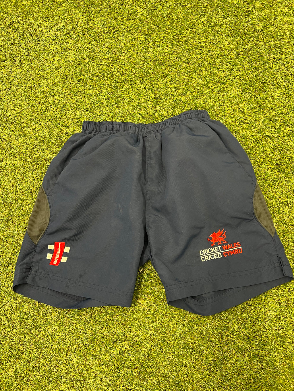 Gray Nicolls kids cricket shorts with Cricket Wales logo on front, black and olive mesh side panels