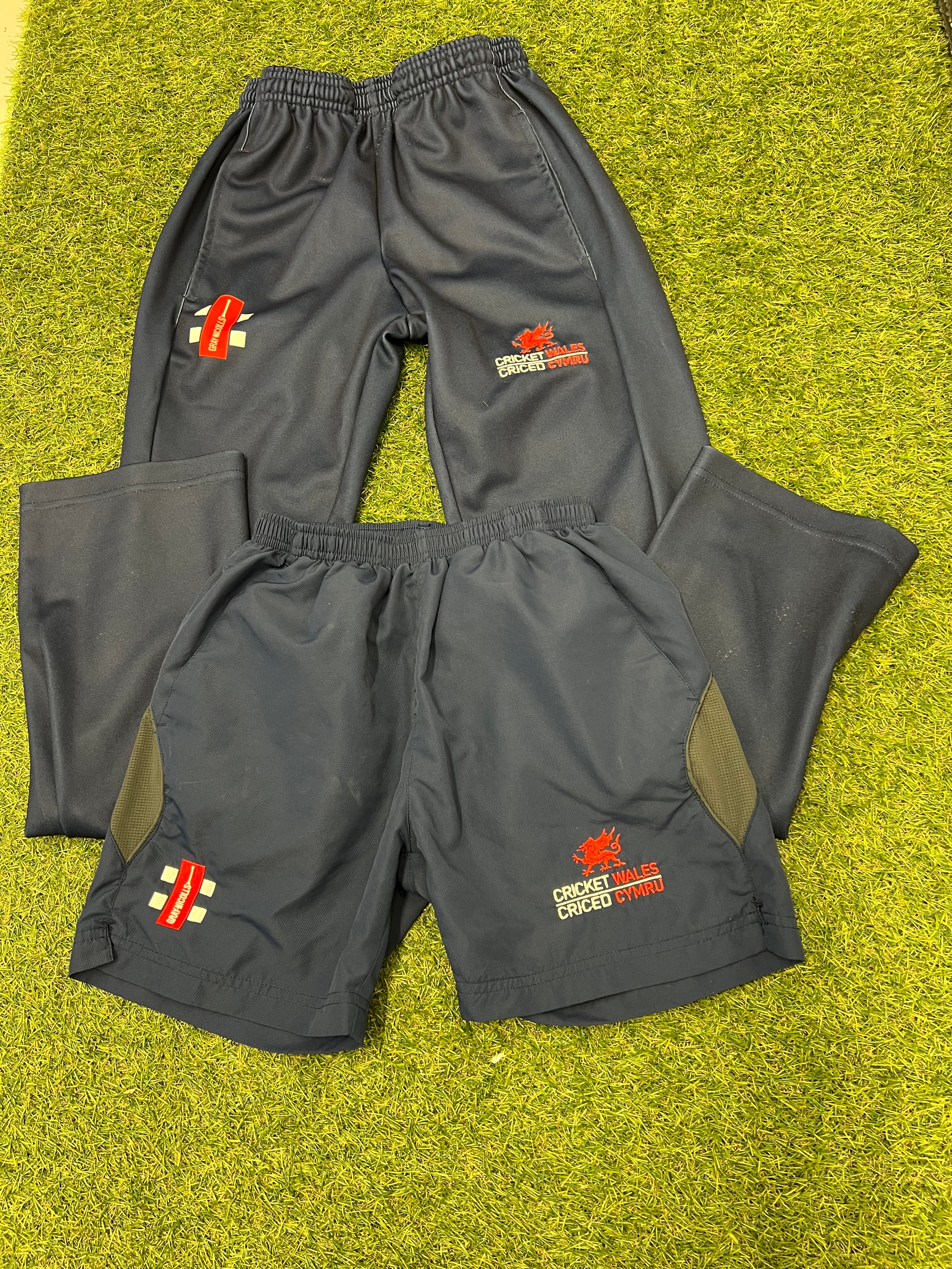 Comparison layout of both gray cricket tracksuit bottoms and shorts side by side on grass background
