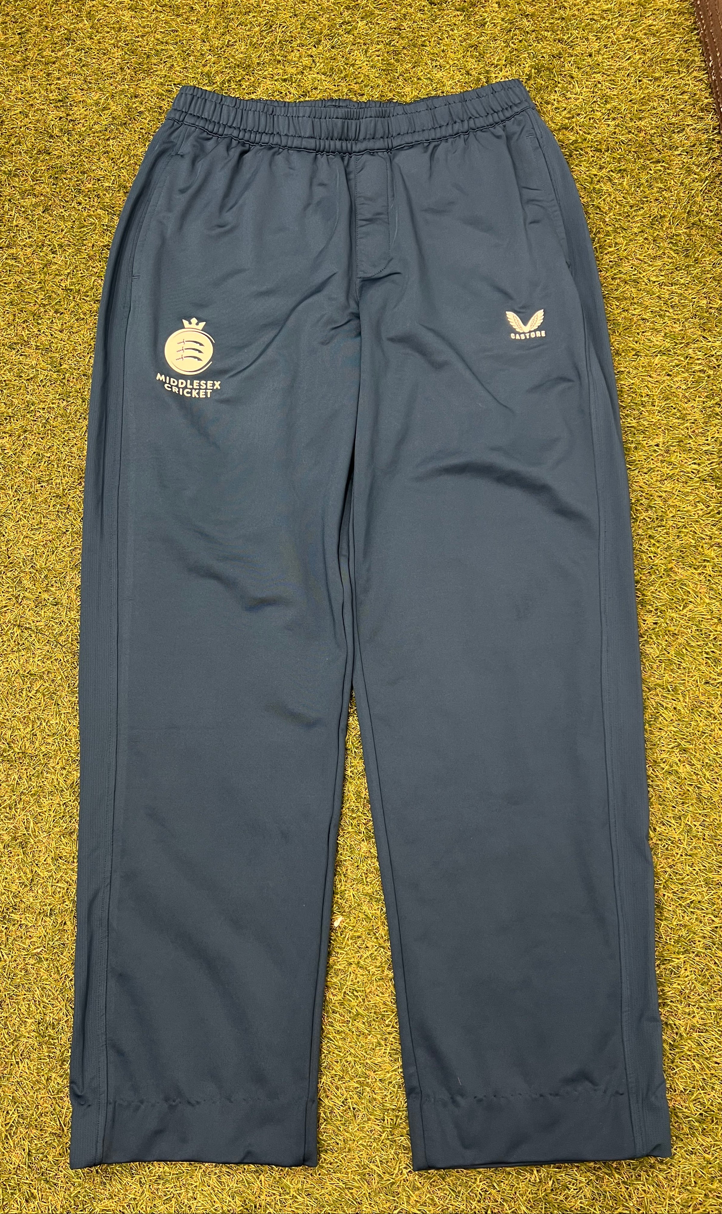 Front view of men's dark navy Castore Middlesex cricket tracksuit bottoms on grass