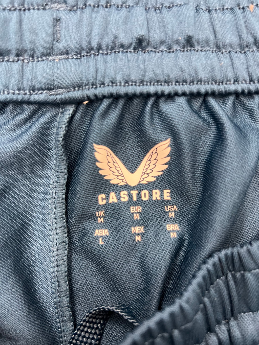 Close-up of inner elastic waistband label inside the dark navy Castore tracksuit bottoms showing size details