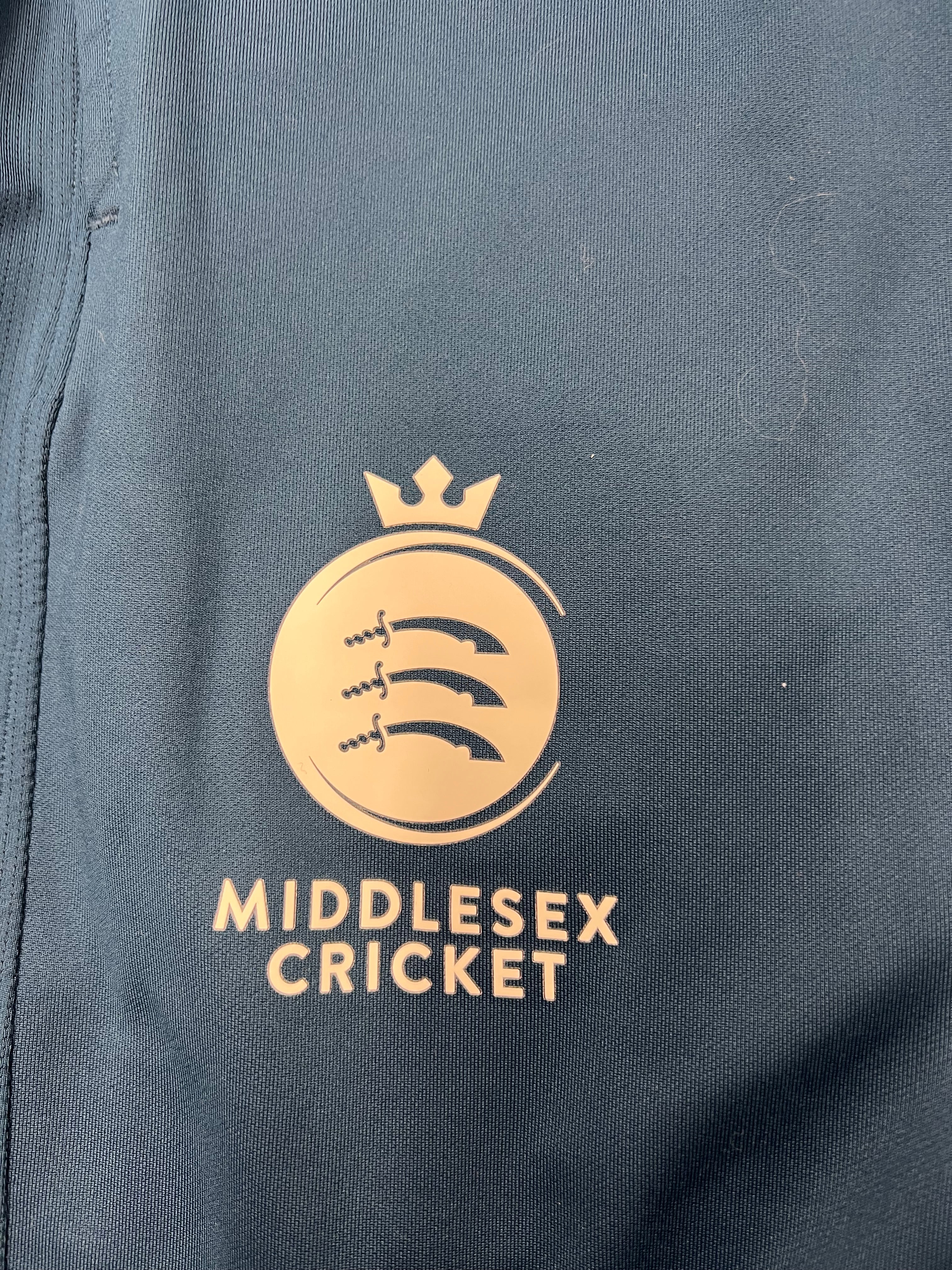 Close-up detail of Middlesex Cricket emblem on the left leg of the navy tracksuit bottoms