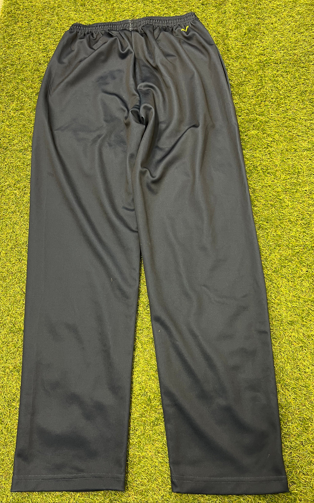 Back view of men's black New Balance tracksuit bottoms on grass showing smooth fabric and elasticated waistband