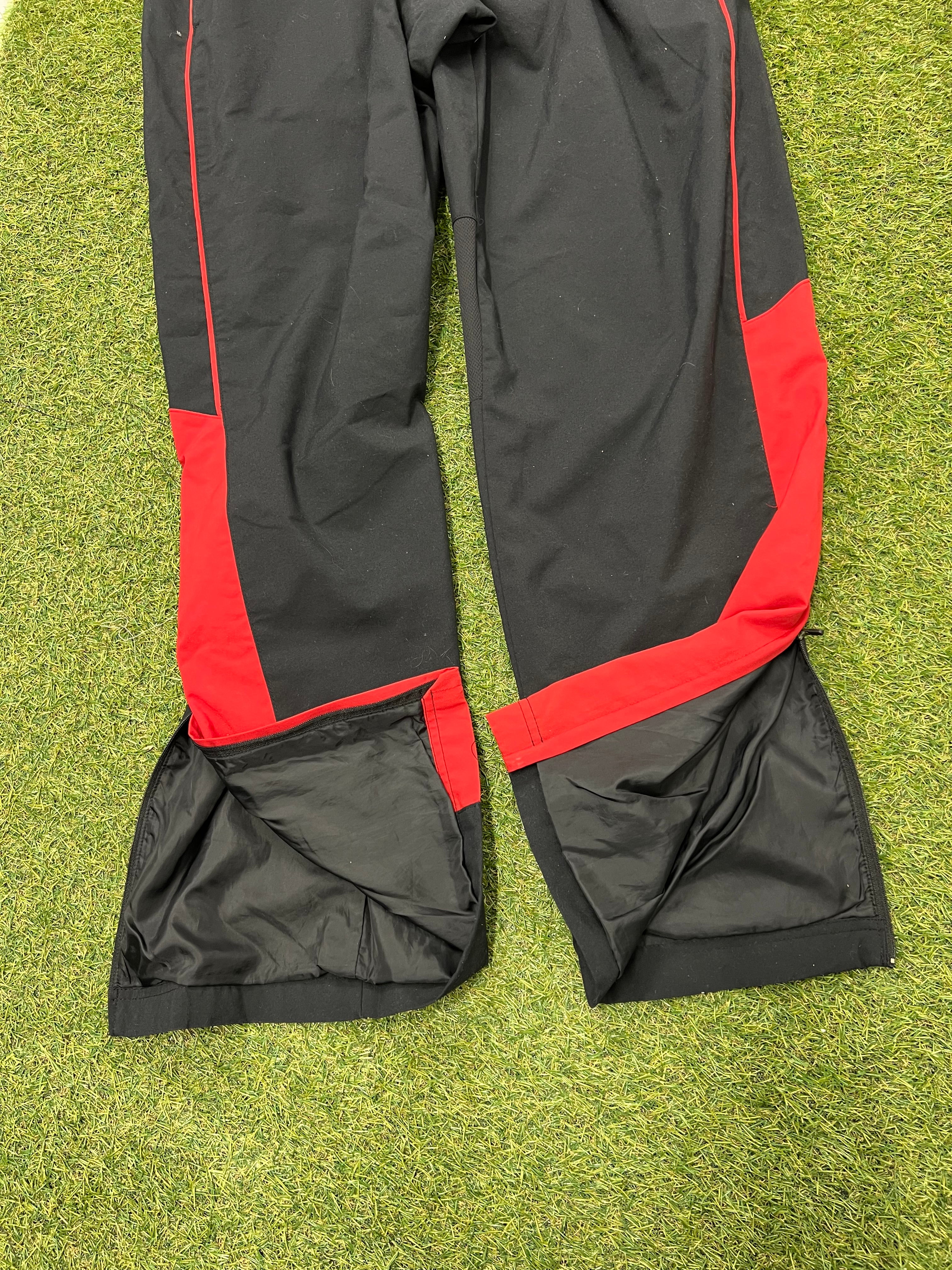 Zip open leg cuffs of men's Nike black and red tracksuit bottoms showing inner lining detail laid flat on grass