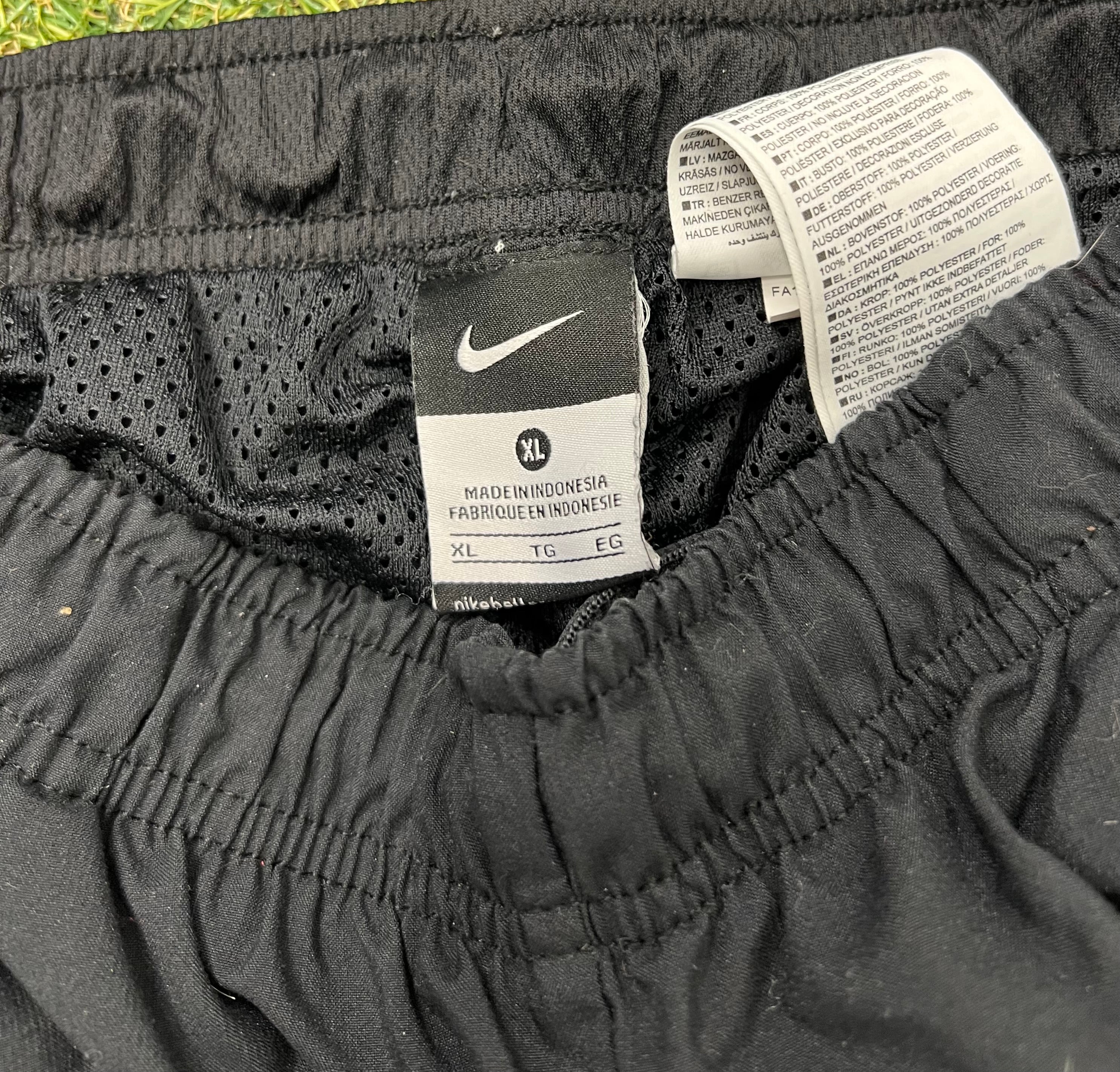 Close-up of elastic waistband and Nike size label inside men's black tracksuit bottoms showing size XL and polyester composition