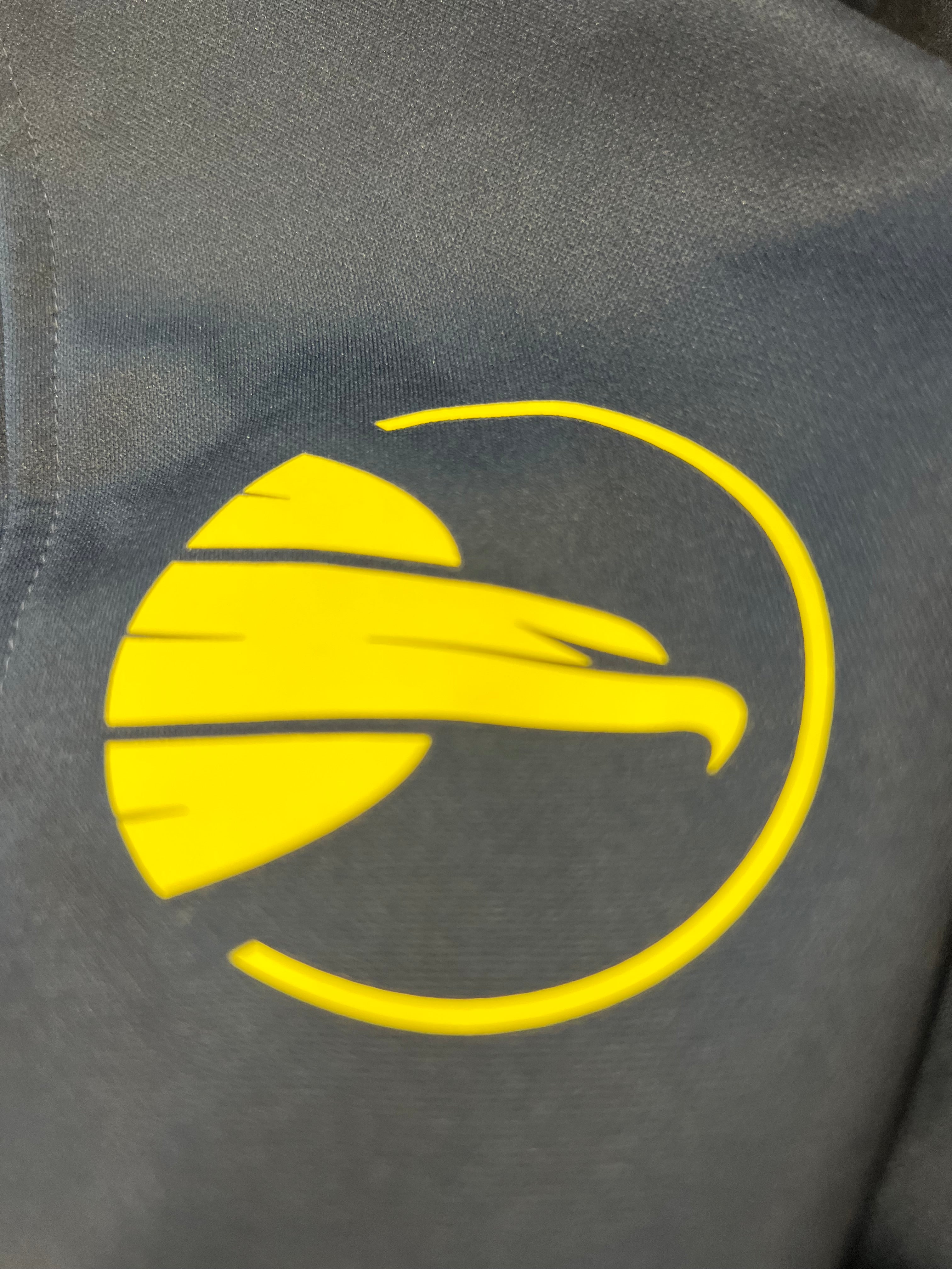 Detailed close-up of yellow bird logo on black fabric of tracksuit bottoms