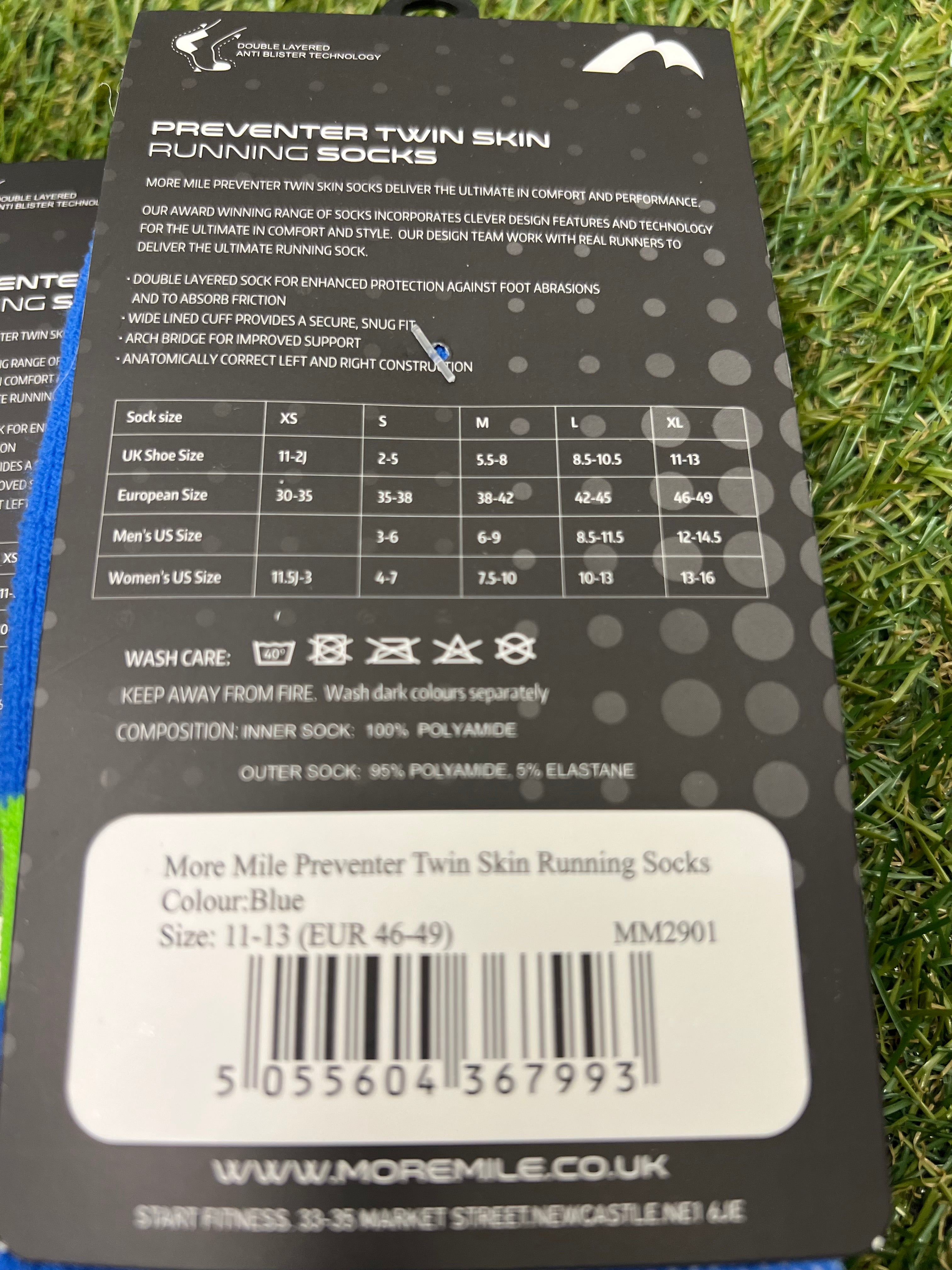 Close-up of product description and size chart on More Mile Preventer Twin Skin Running Socks packaging on grass background