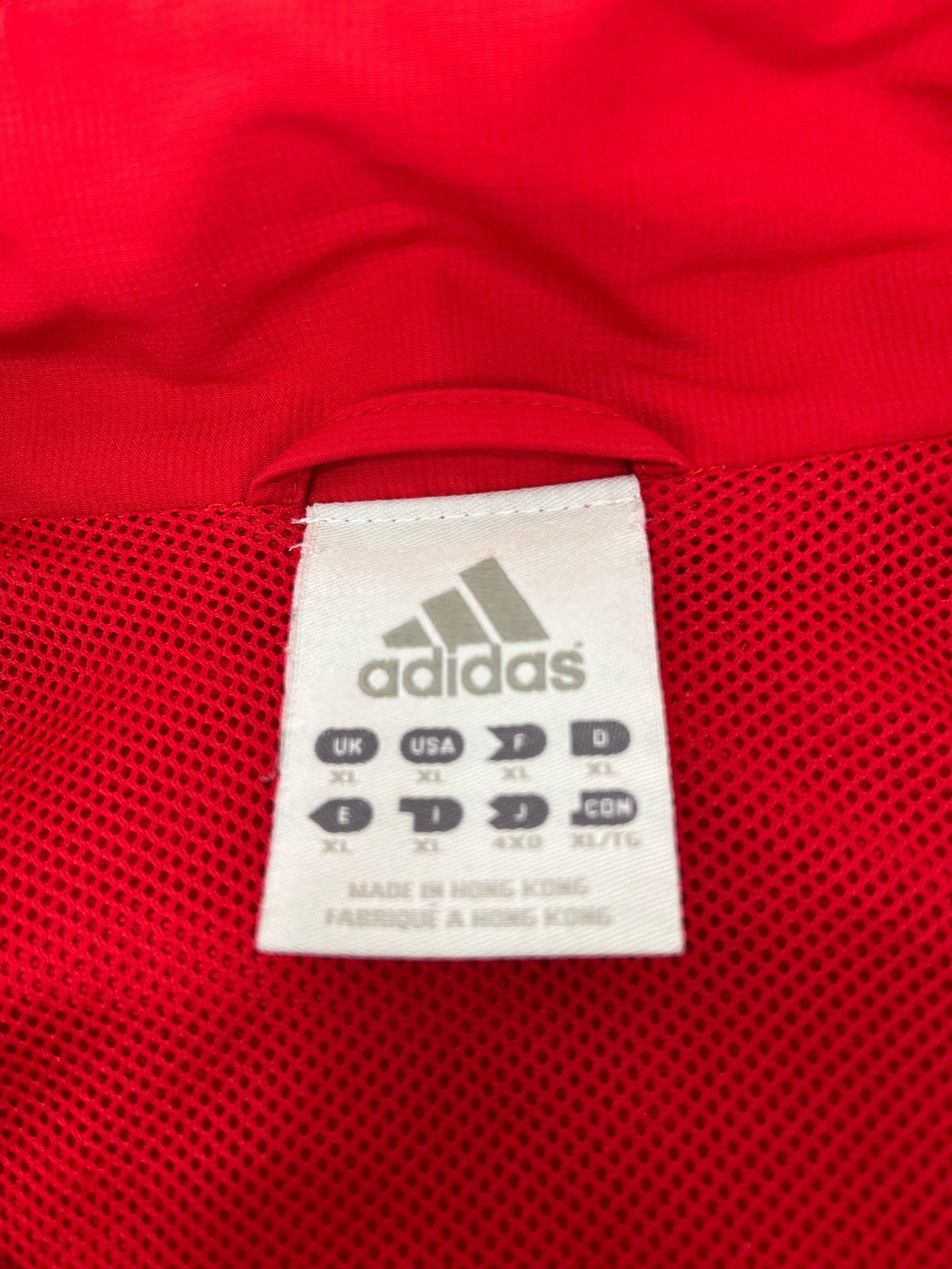 Close-up of Adidas size label inside red men’s lightweight jacket showing multiple international sizes