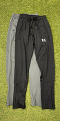 Black and grey Under Armour tracksuit trousers laid out side by side on grass