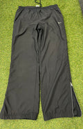 Front view of Nike black loose fit track pants with elastic waistband and zipped side ankle detail on grass surface