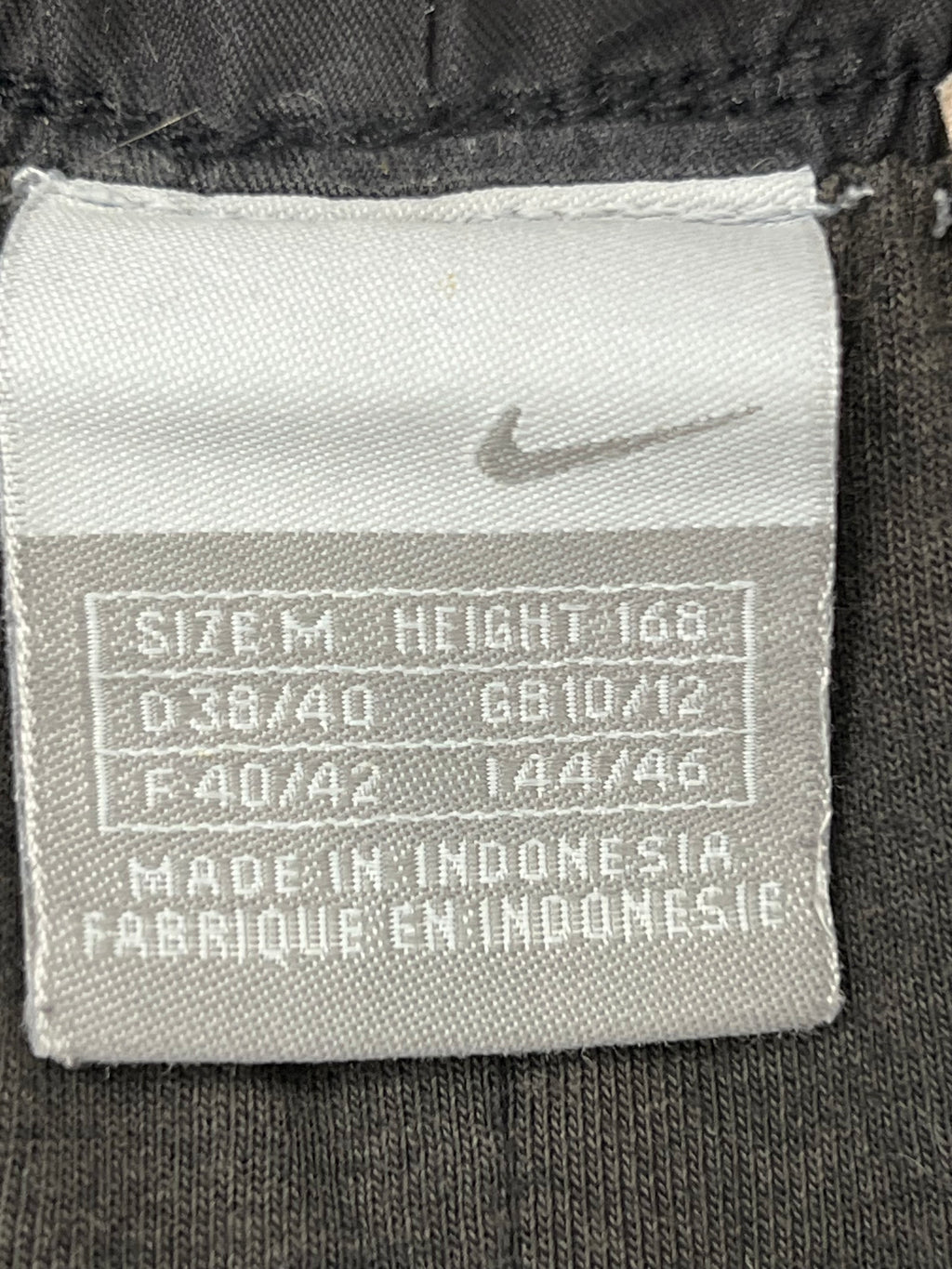 Close-up shot of Nike size label inside black track pants indicating medium size and made in Indonesia