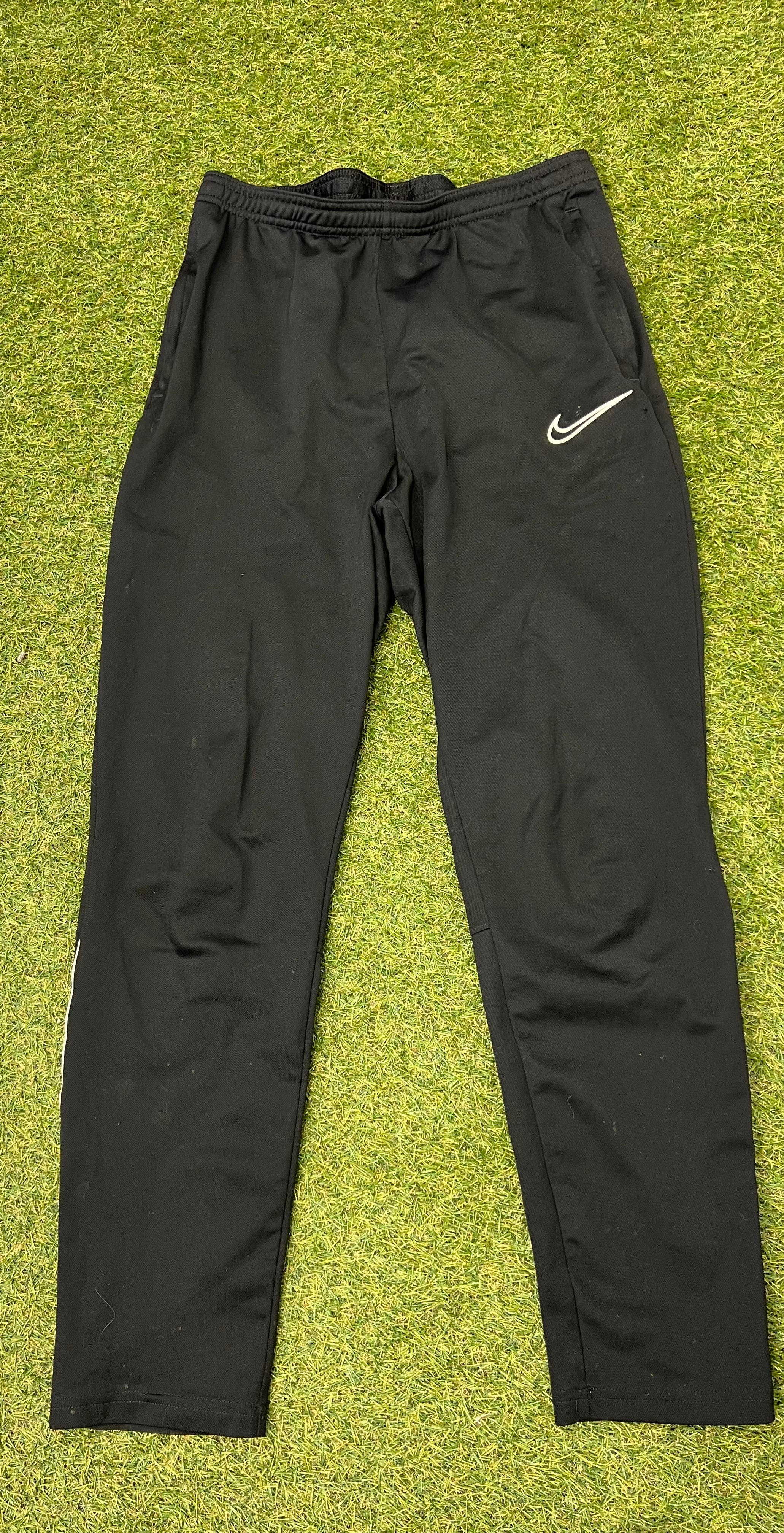 Front view of black Nike Dri-FIT tracksuit bottoms with elastic waistband and Nike swoosh logo on left thigh