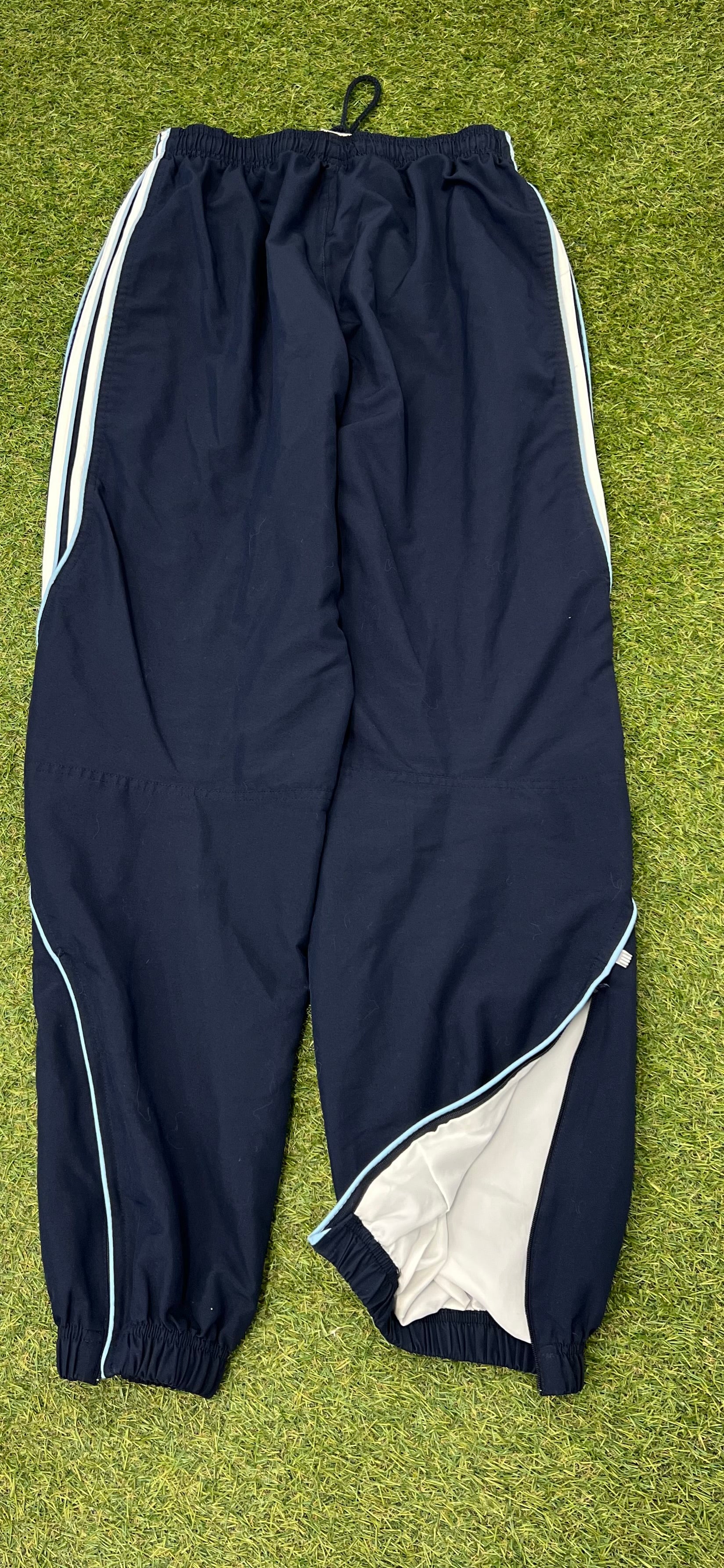 Back view of men's Adidas navy tracksuit bottoms showing white lining and piping details on grass