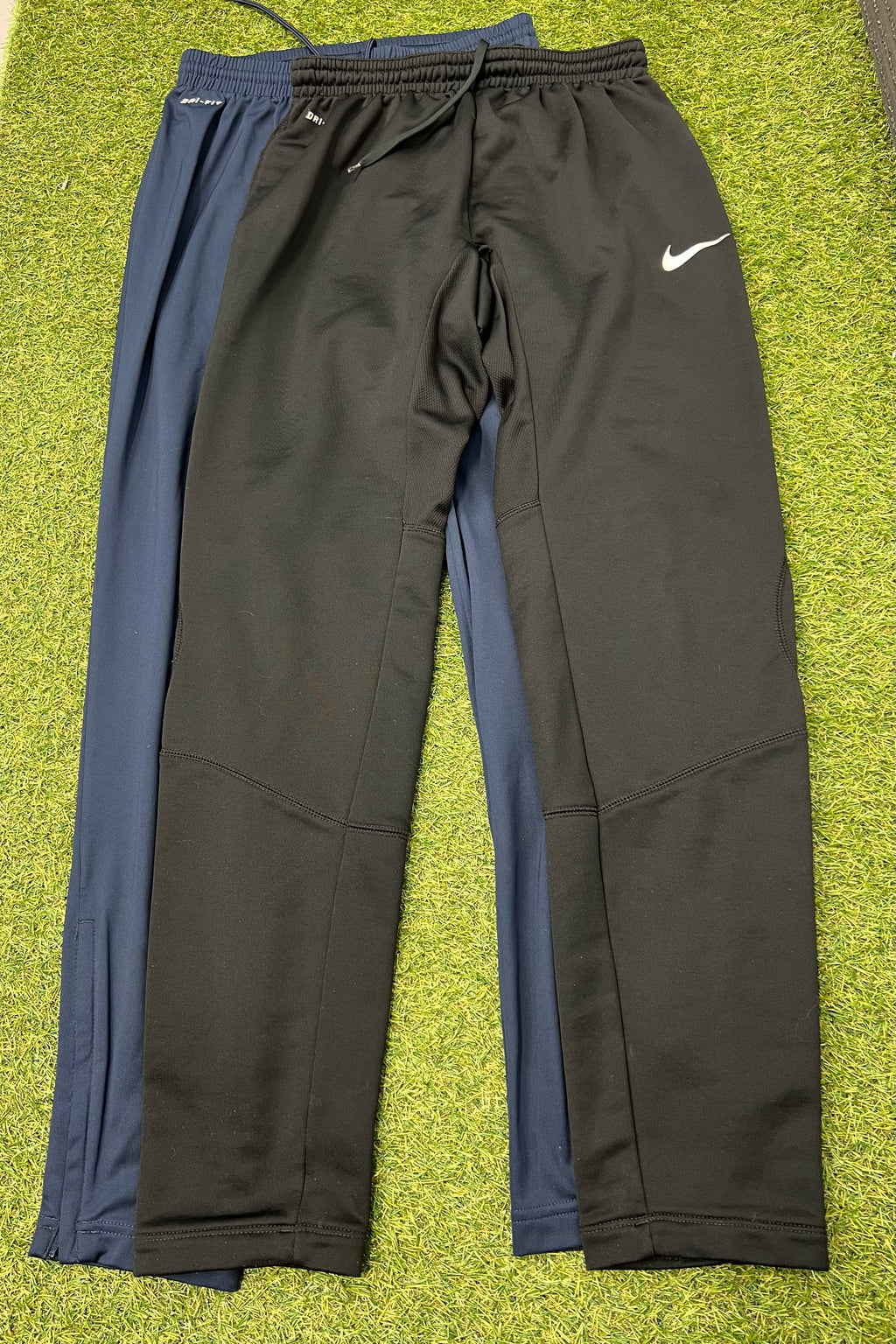 Pair of Nike Dri-FIT tracksuit bottoms in black and navy laid flat on grass surface