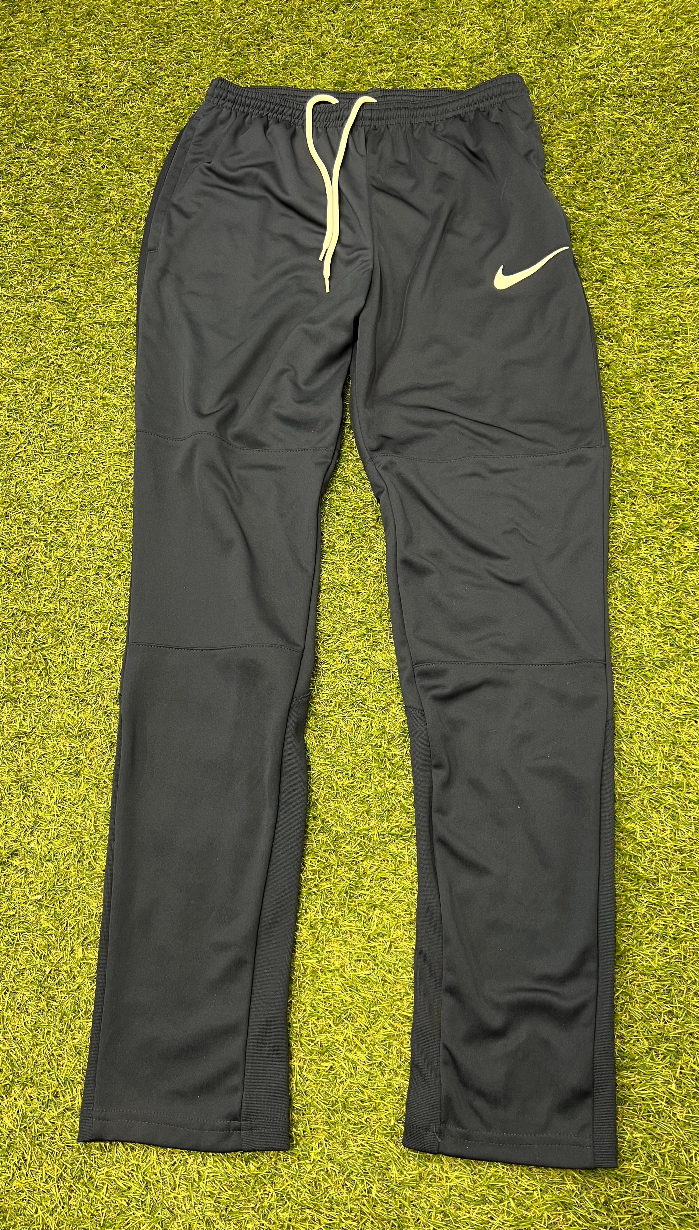 Black Nike Dri-FIT tracksuit bottoms with white drawstring and logo displayed on grass