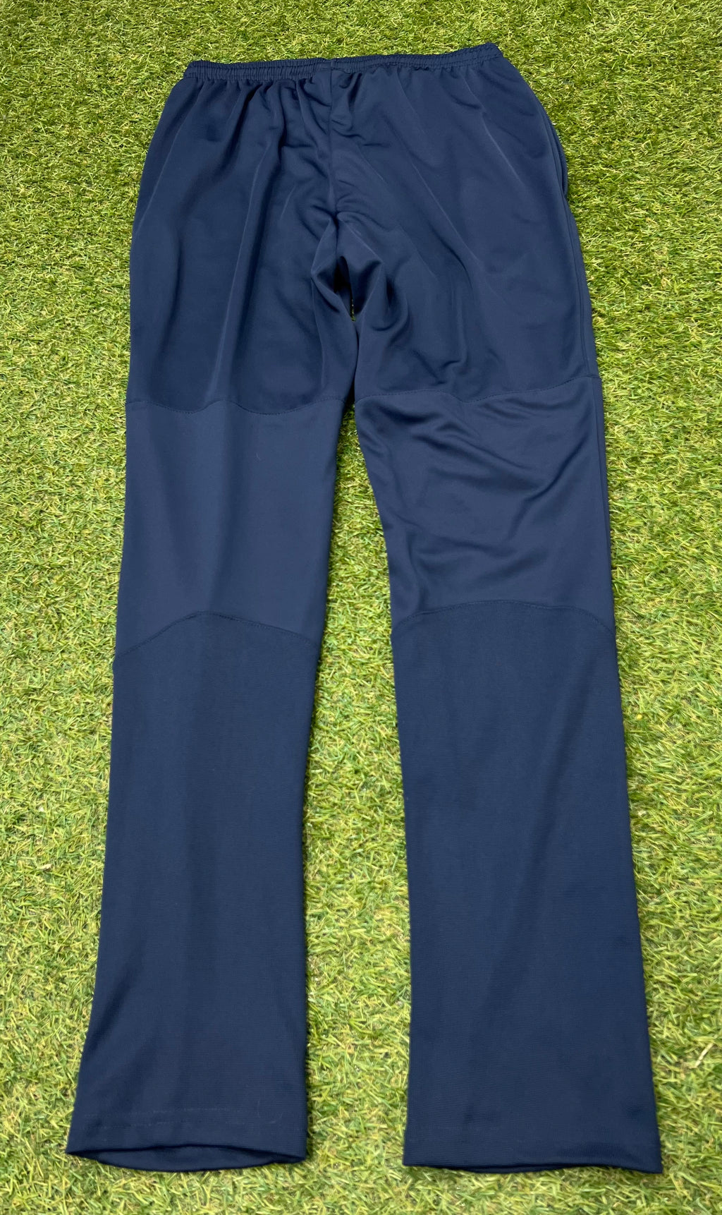 Navy Nike Dri-FIT tracksuit bottoms showing rear view on grass