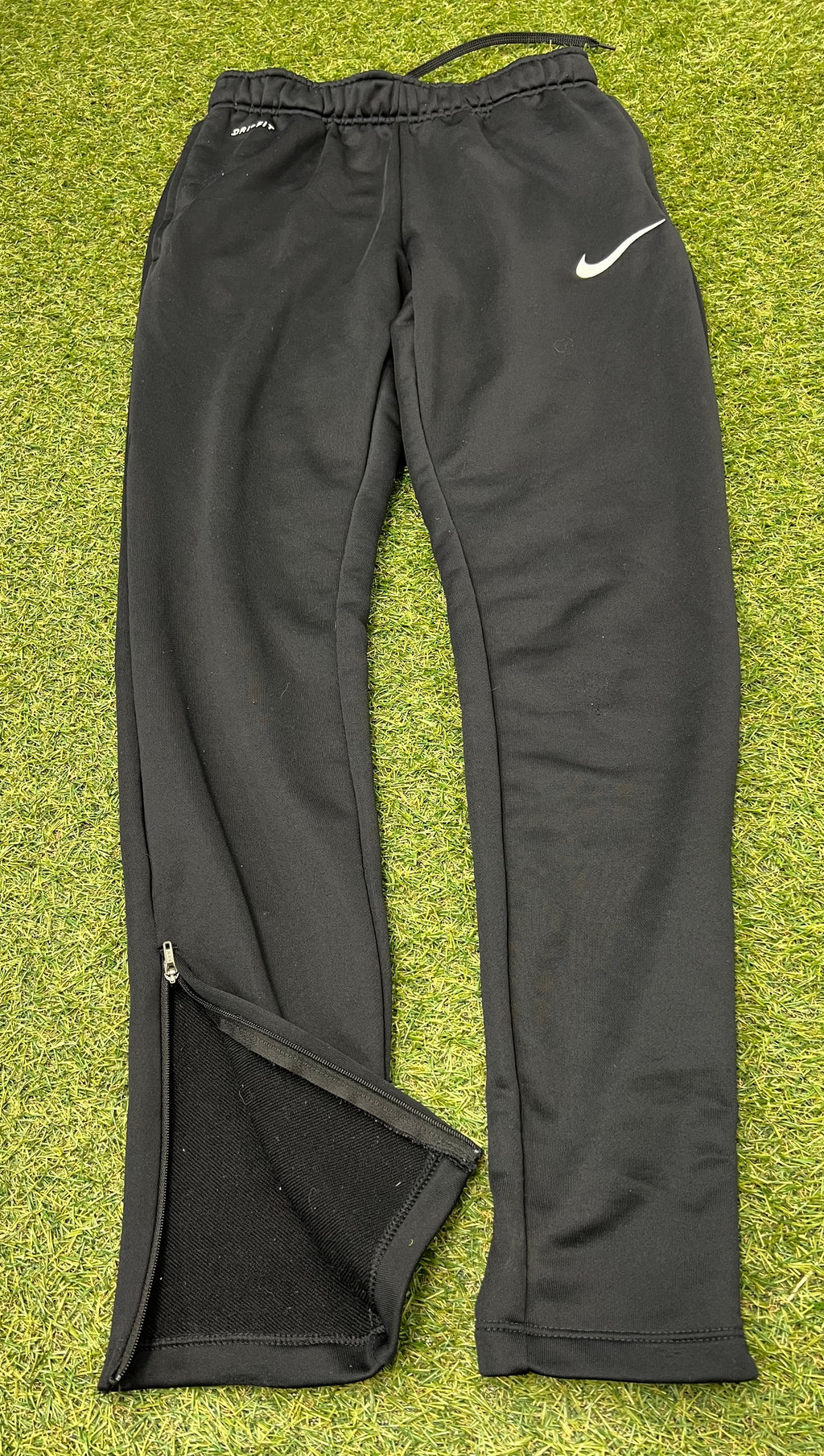 Front view of black Nike Dri-FIT tracksuit bottoms with logos on grass