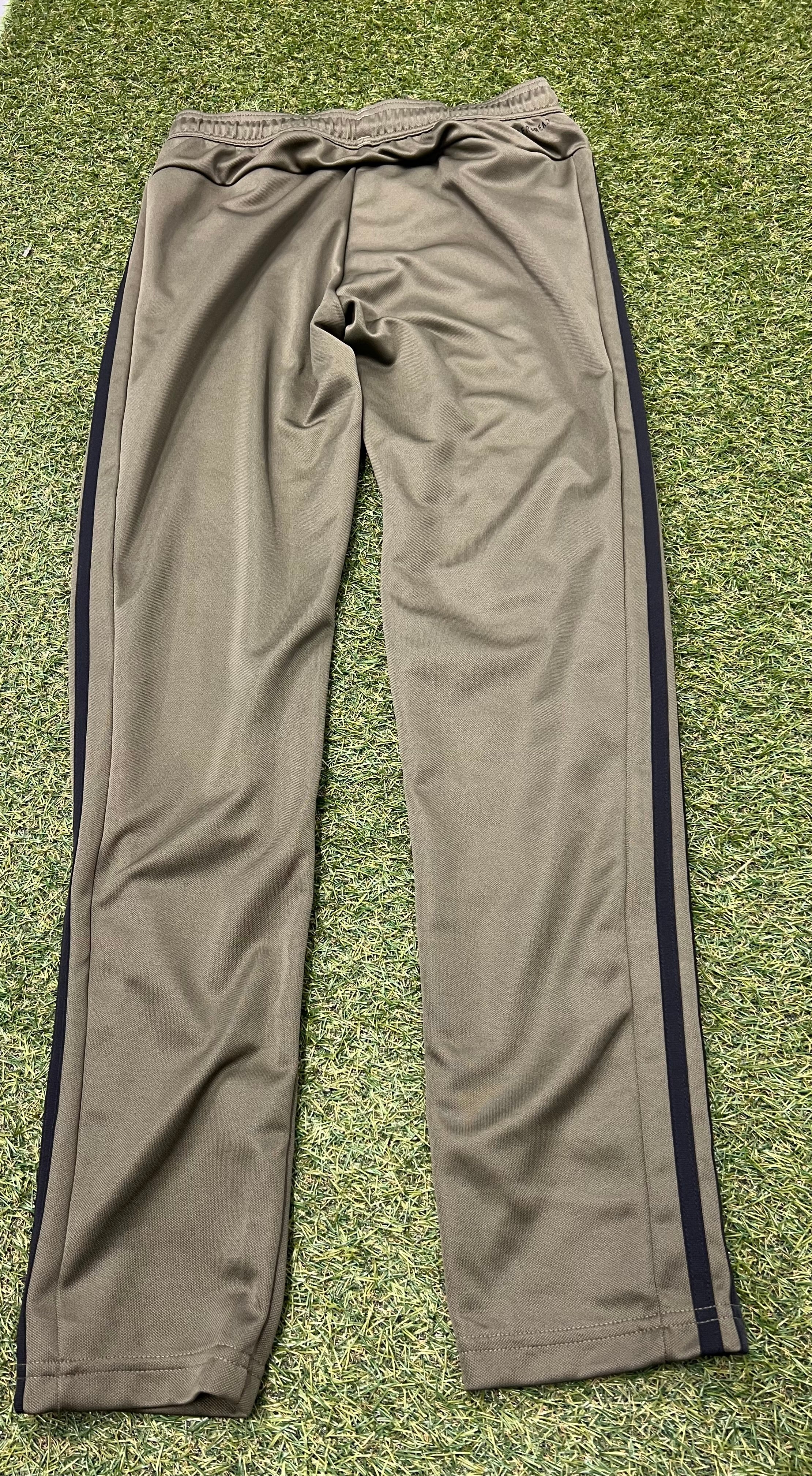 Back view of men's khaki tracksuit bottoms showing clean design with black stripes down sides, laid flat on grass.