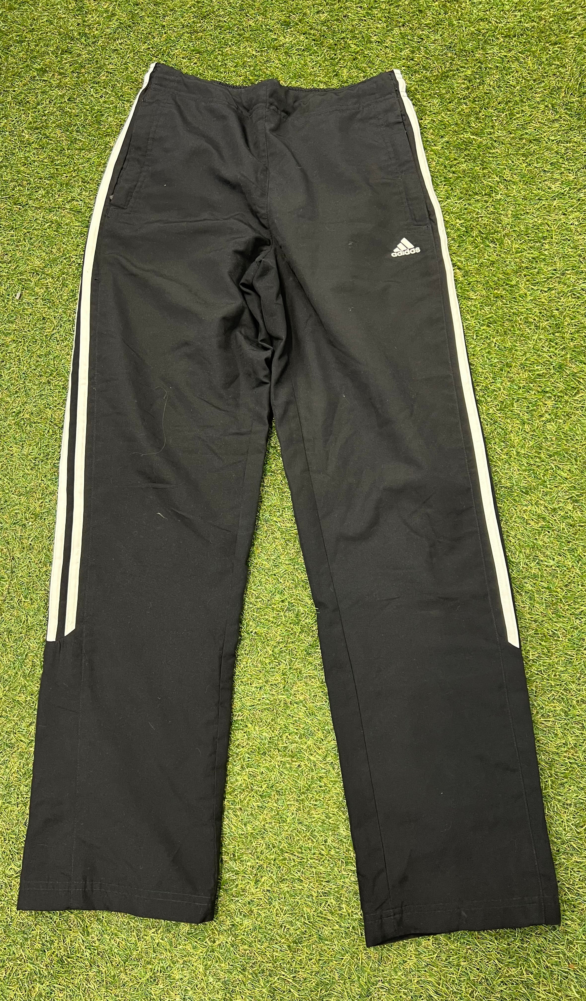 Front view of black adidas women's tracksuit bottoms with white side stripes laid flat on grass background