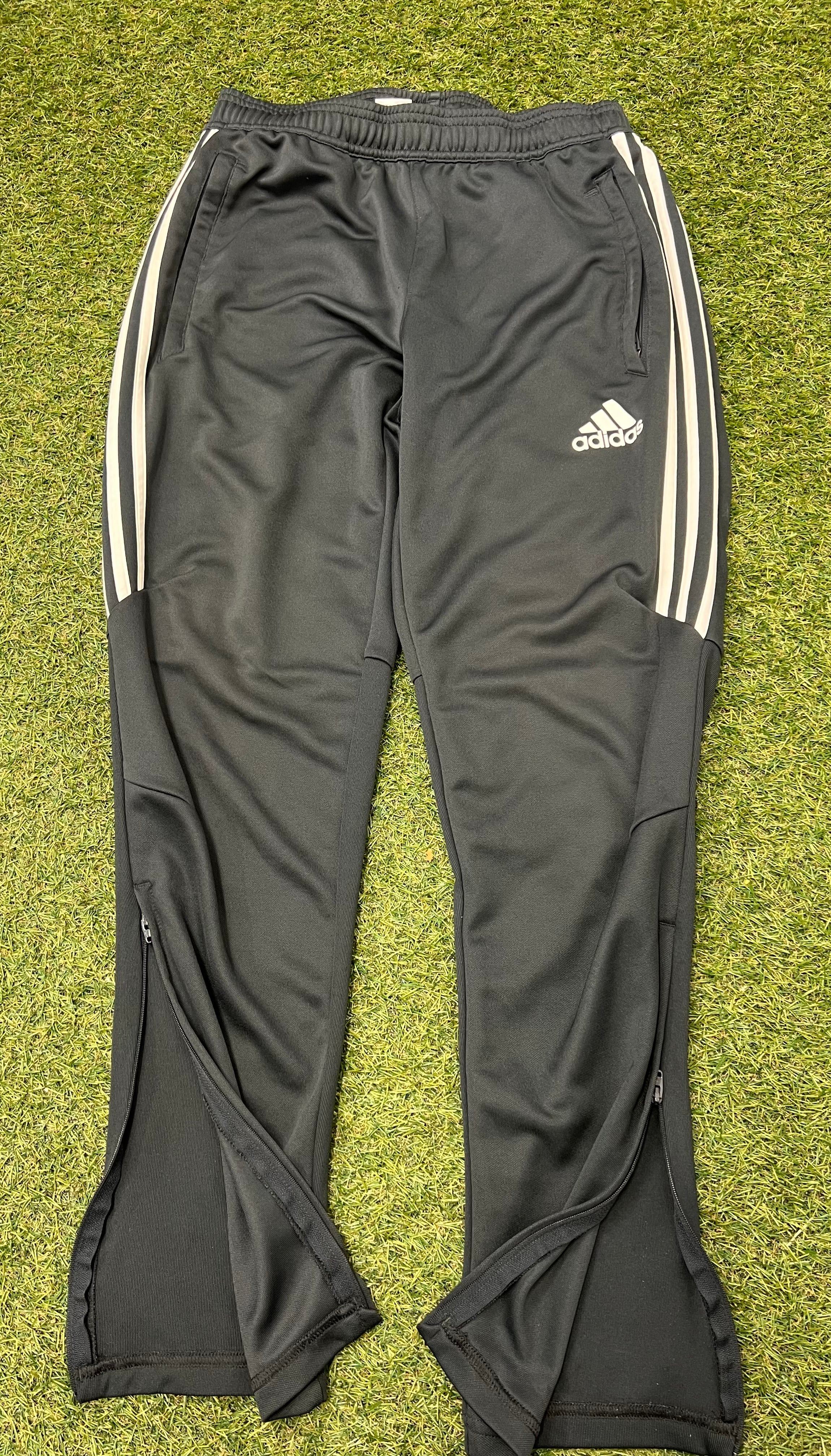 Front view of black Adidas Climacool men's tracksuit bottoms with white side stripes and zippered ankle vents laid flat on grass