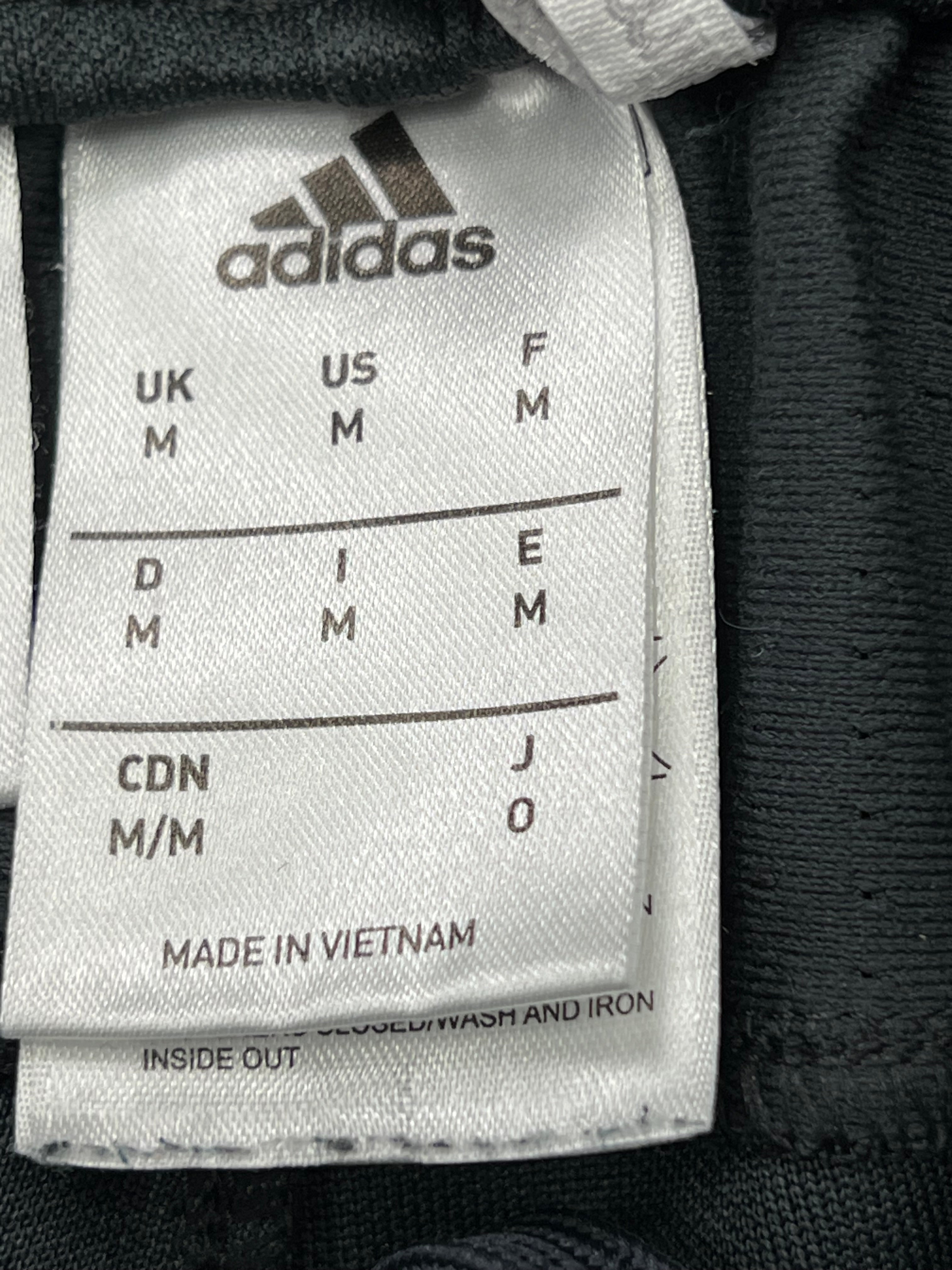 Close-up of Adidas size label in black and white showing size Medium and manufacture details inside the waistband