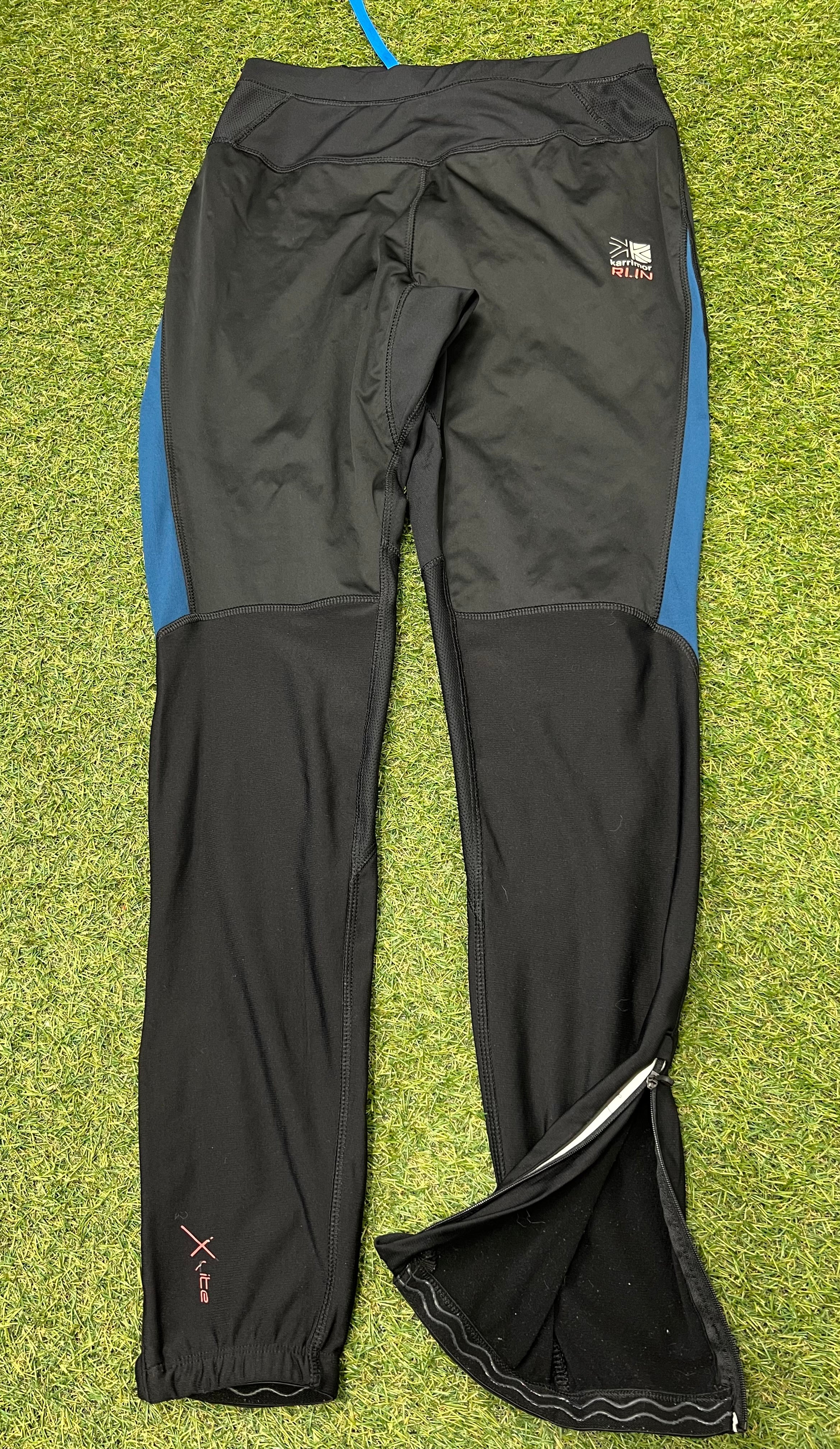 Front view of black Karrimor X Lite running tights with blue side panels and zipped ankle cuffs laid flat on grass